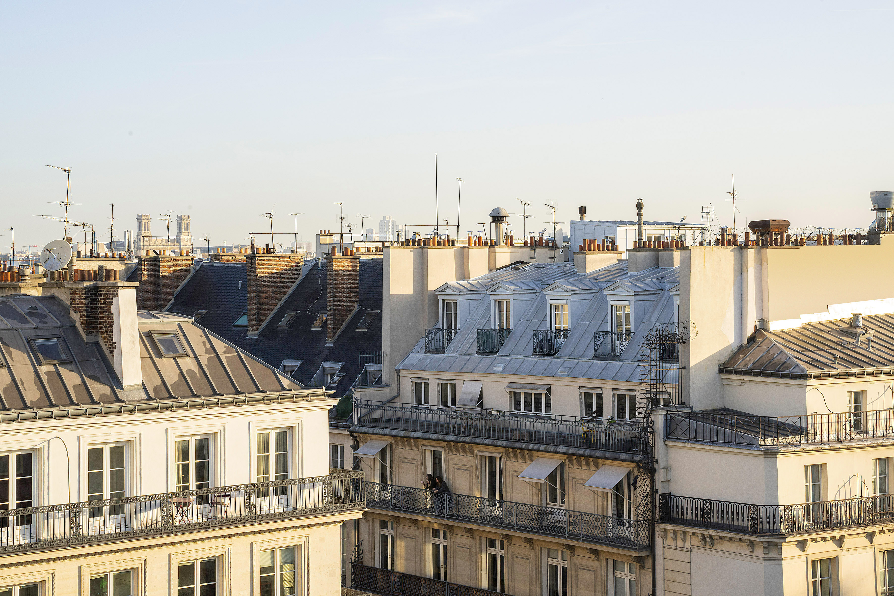 Golden hour on Paris rooftops, Haussmann buildings with chimneys and balconies.