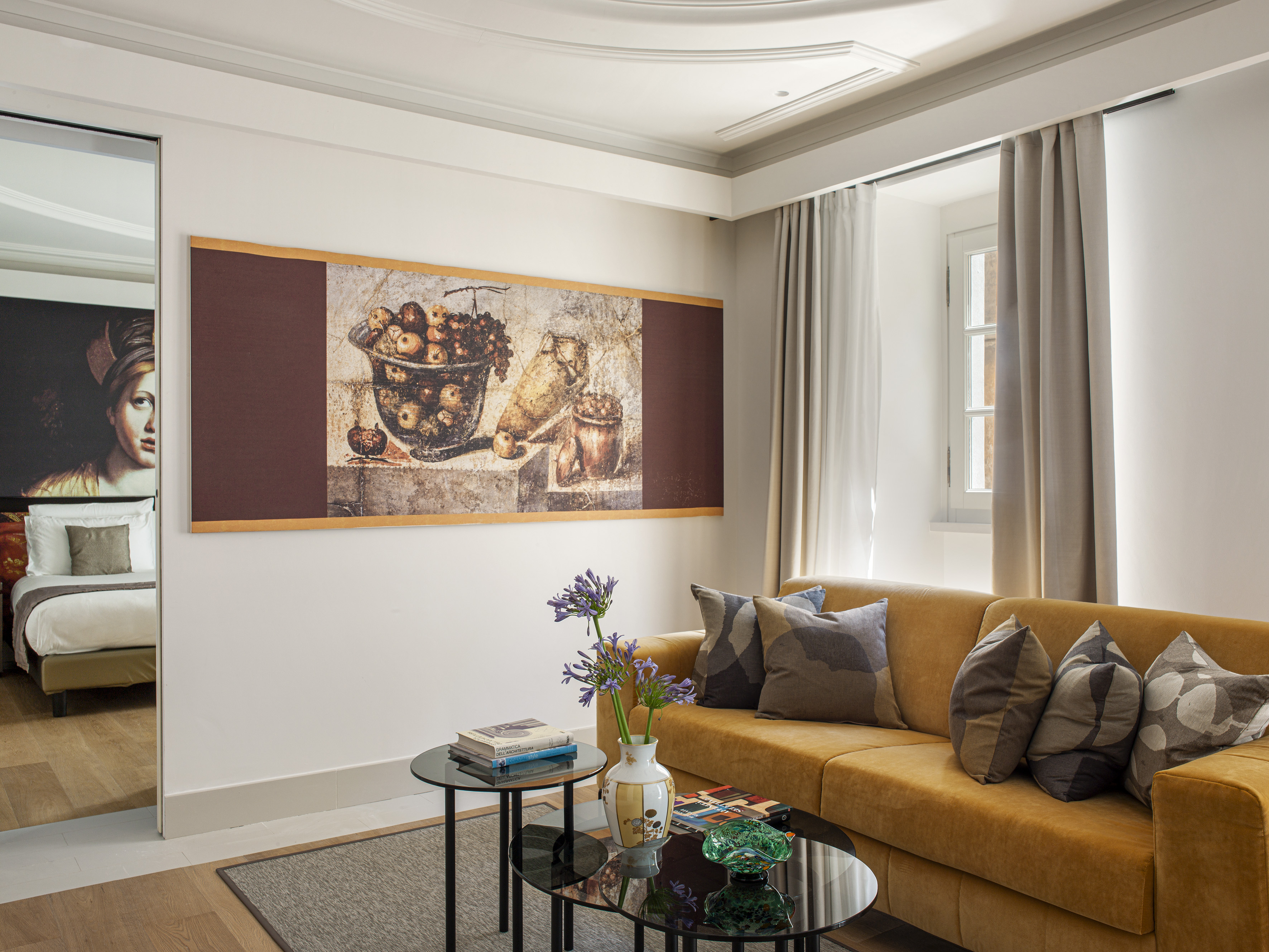 Modern hotel suite with mustard sofa, still life painting, glass tables.
