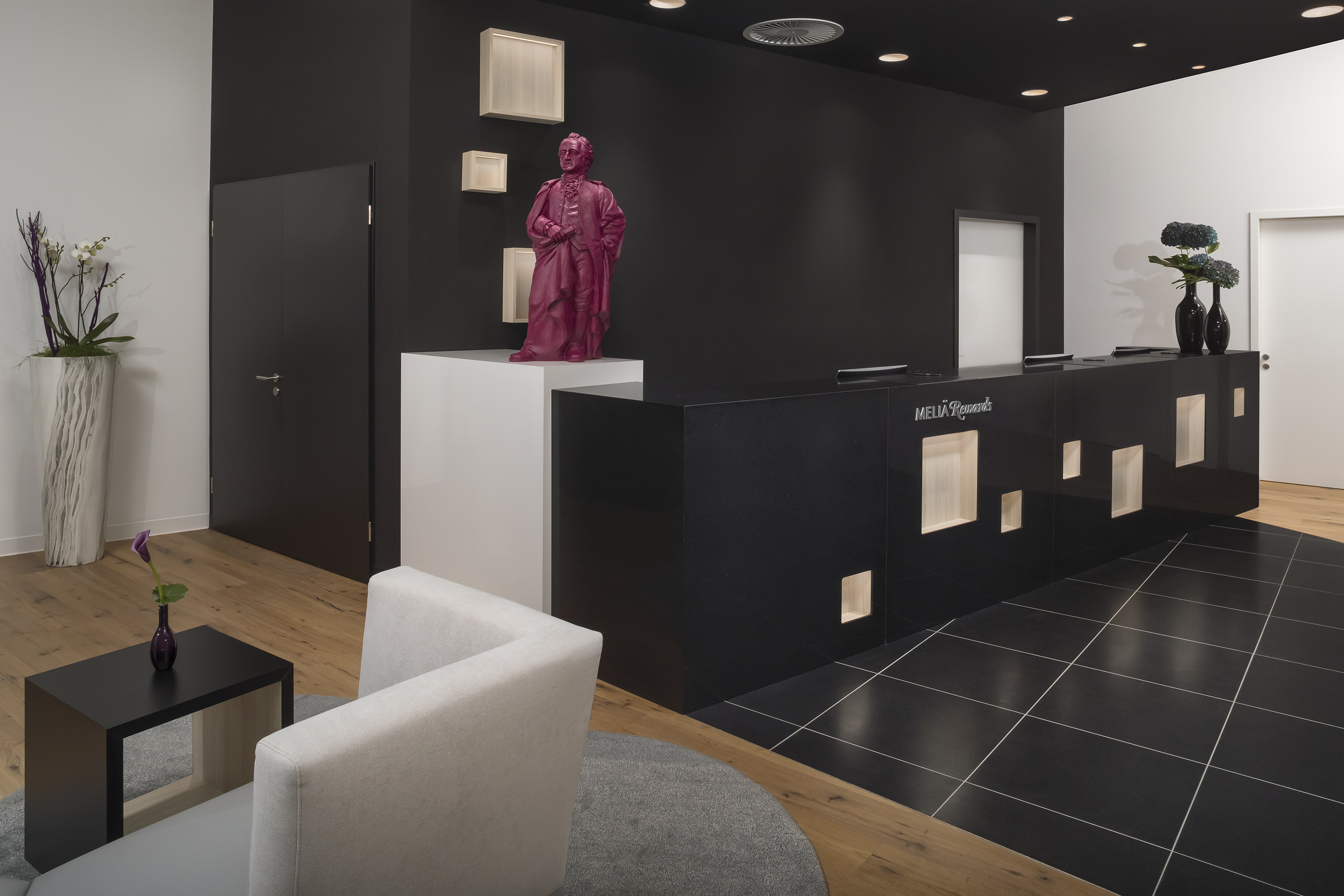 Stylish hotel lobby with black reception desk, pink statue, wood and tile flooring.