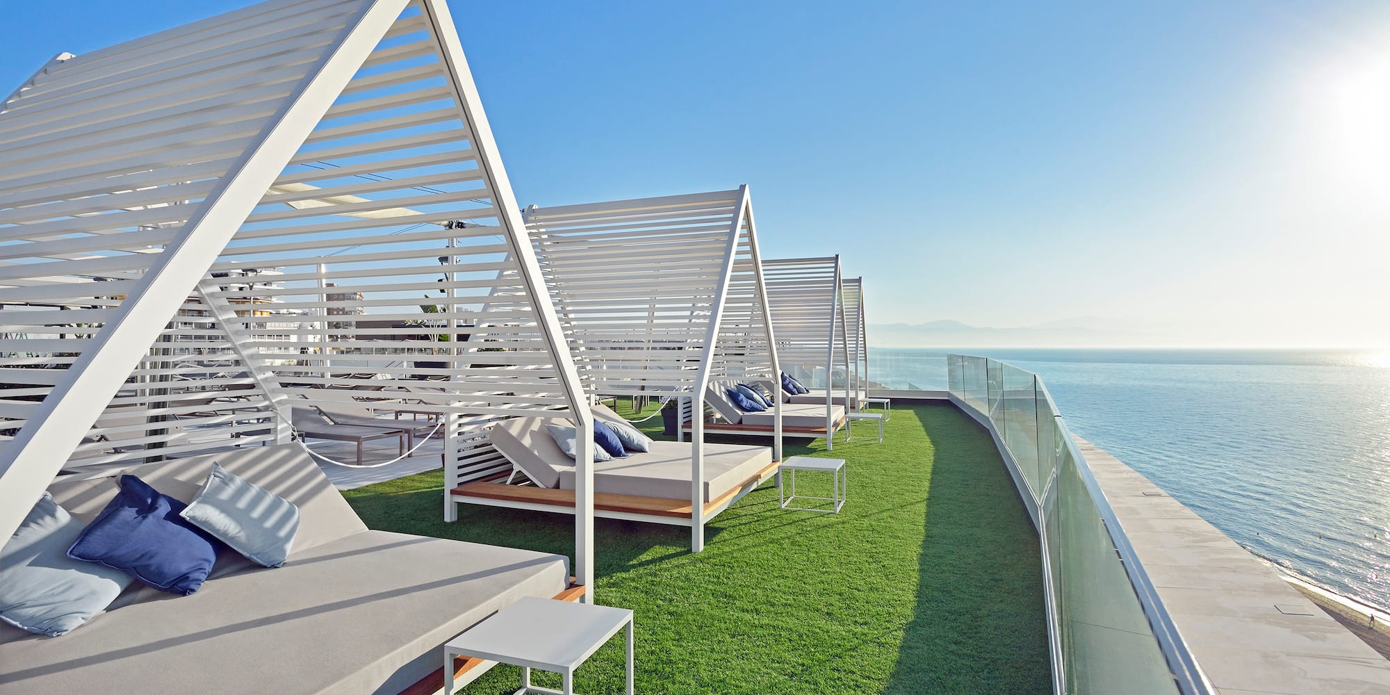 a deck with white beds and a glass railing overlooking the water
