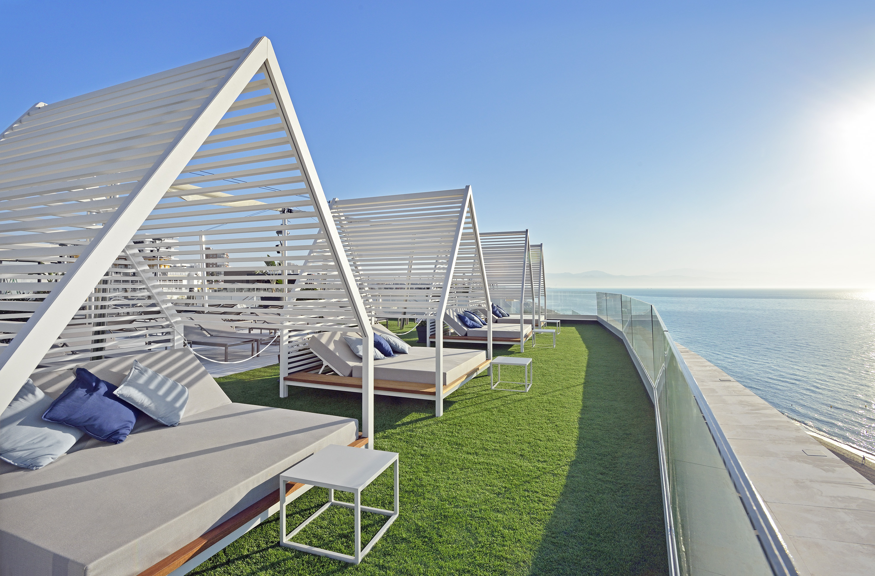 a deck with white beds and a glass railing overlooking the water