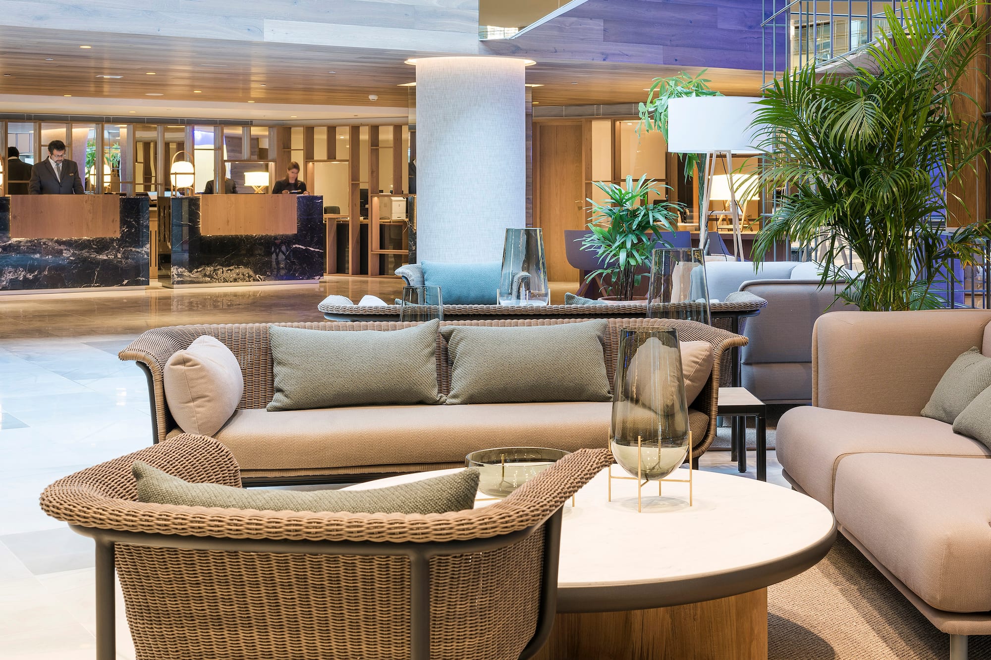 Modern hotel lobby with wicker sofas, reception desk, and lush green plants.
