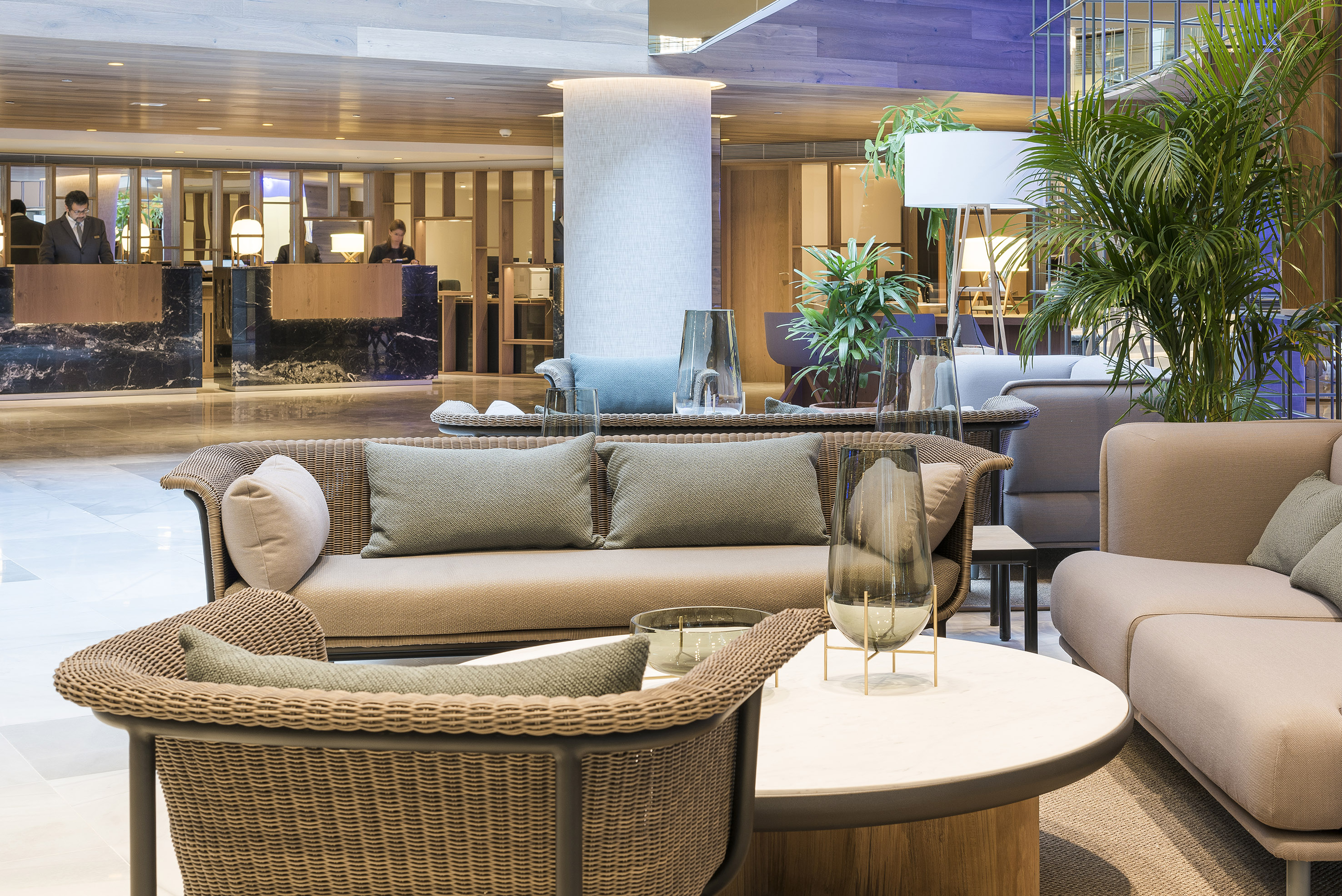 Modern hotel lobby with wicker sofas, reception desk, and lush green plants.
