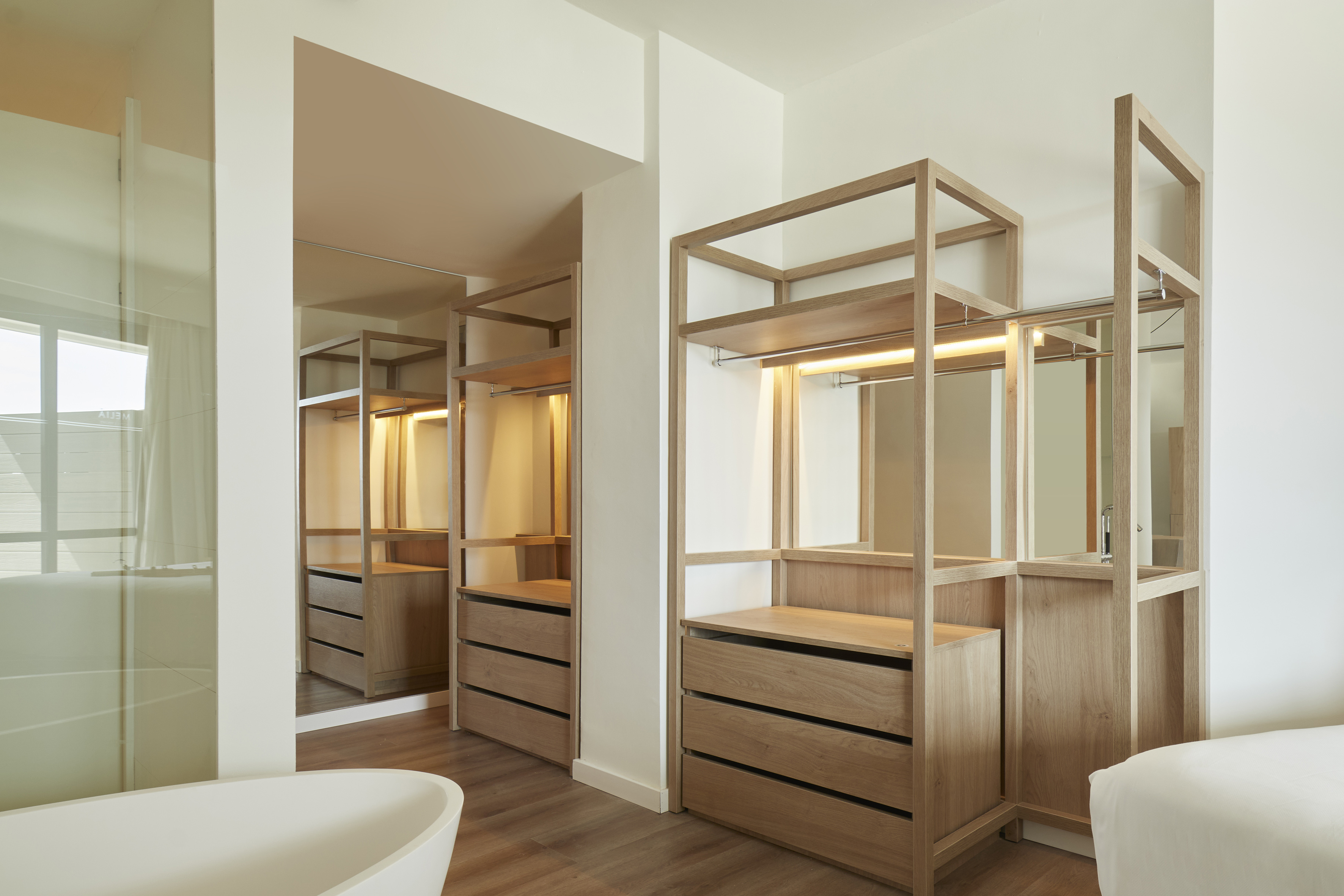 Modern open wooden closet system with drawers, mirrors, and lighting.