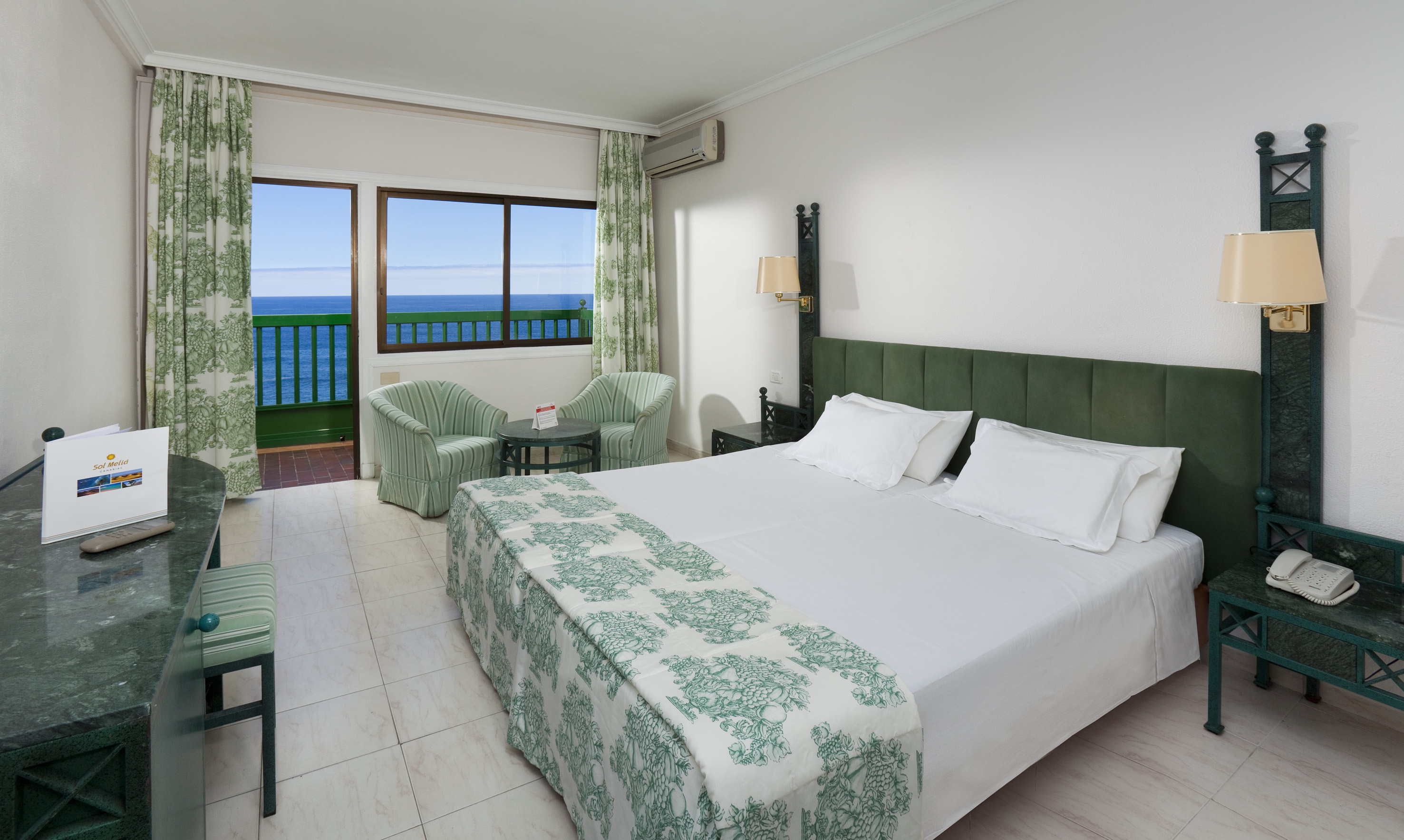 Hotel room with ocean view, double bed, green accents, and balcony.