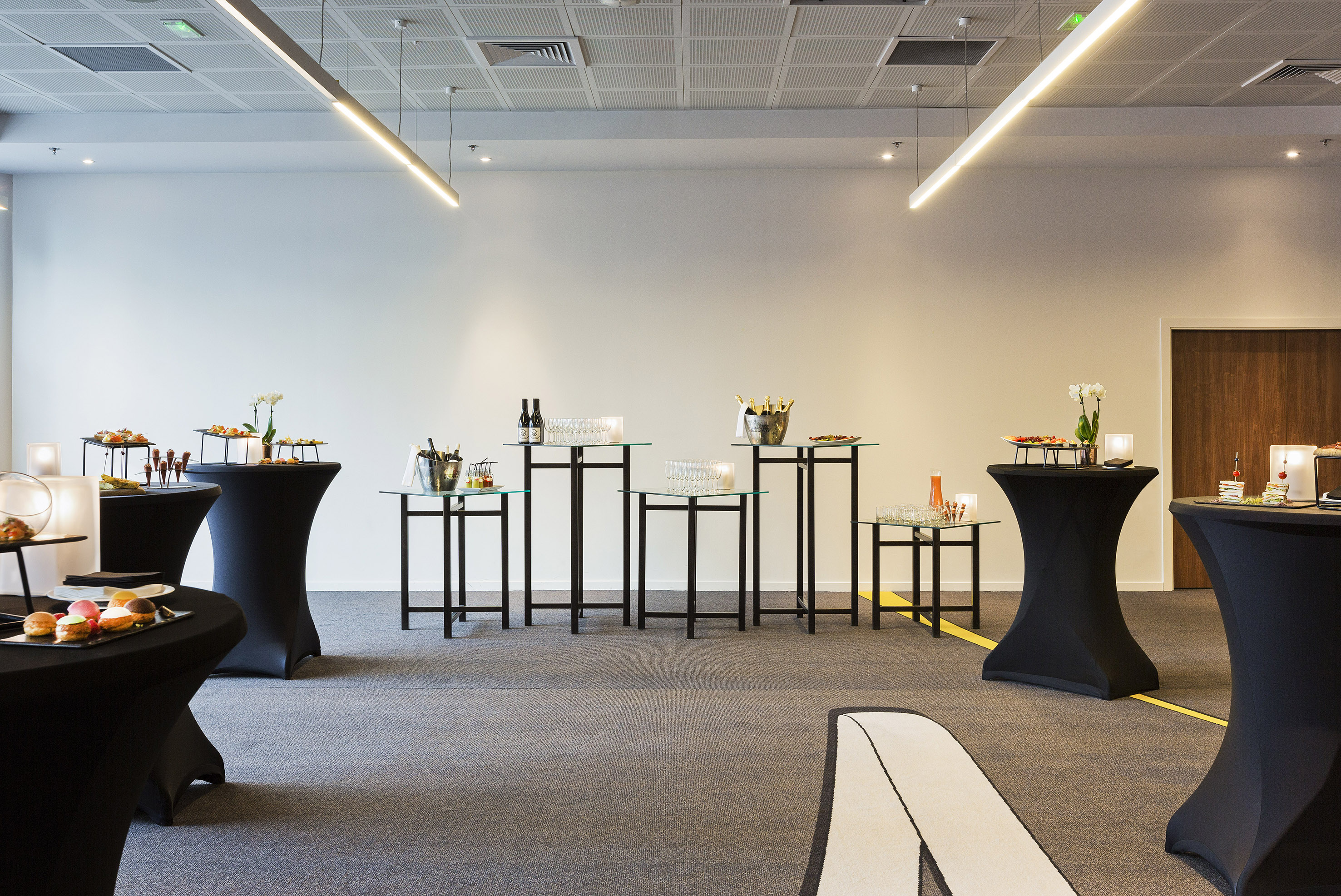 Modern event room catering setup with cocktail tables, appetizers, and drinks.