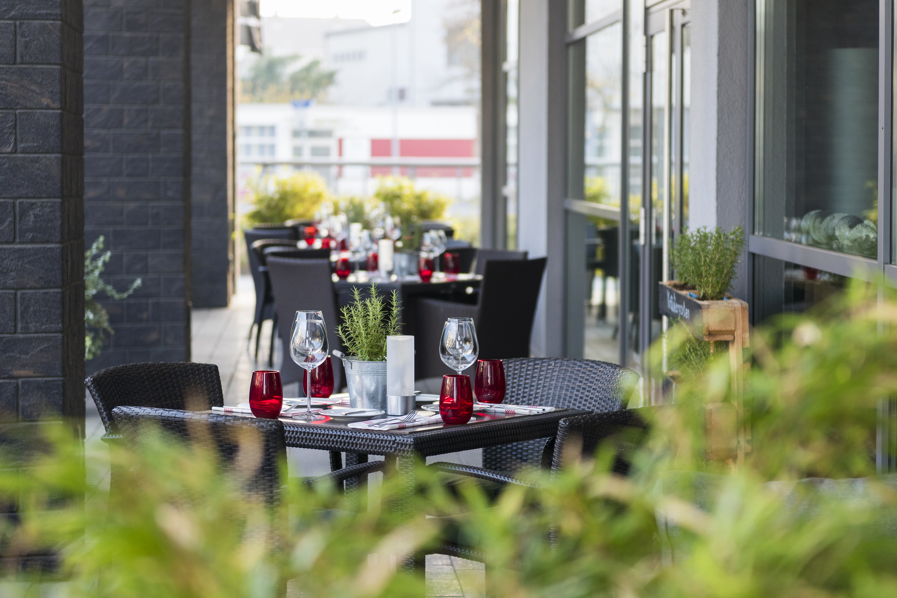 Restaurant patio tables set with red glasses, wine glasses, and green herbs.