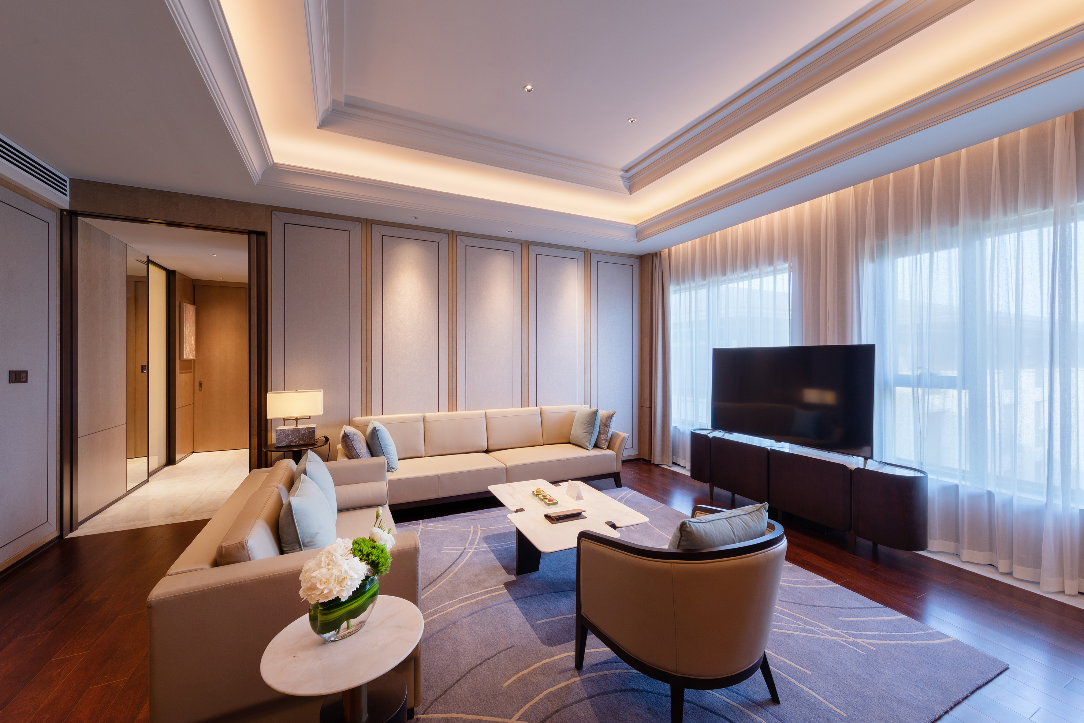 Modern luxury living room with beige couches, elegant design, and ambient lighting.