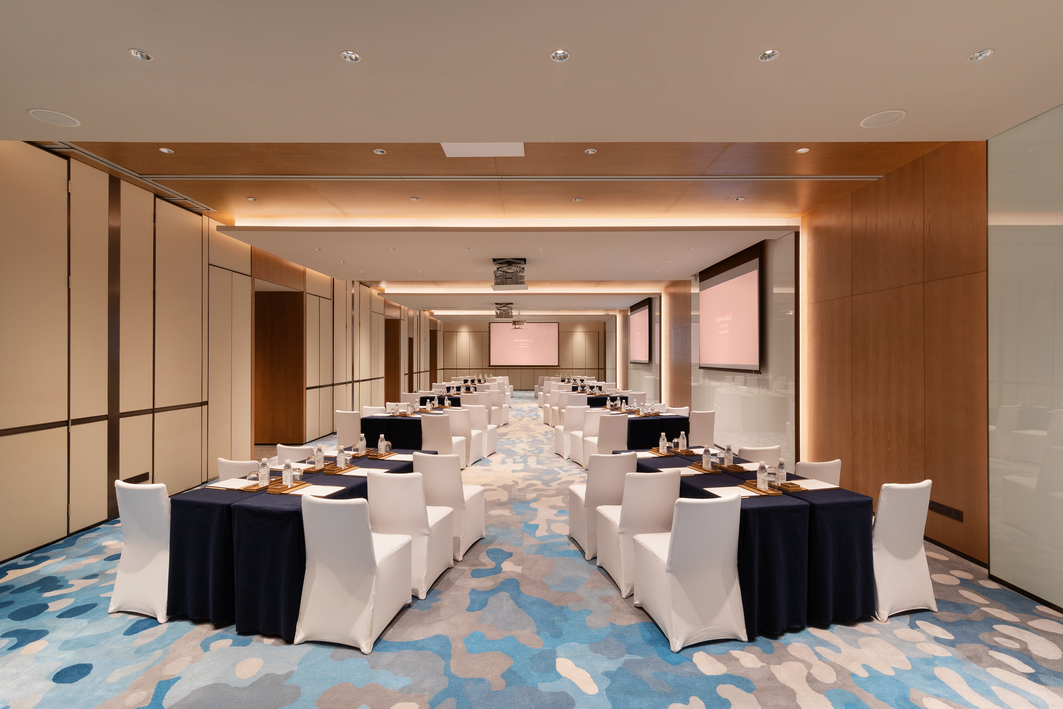 Spacious modern meeting room with tables, white chairs, and projection screens.