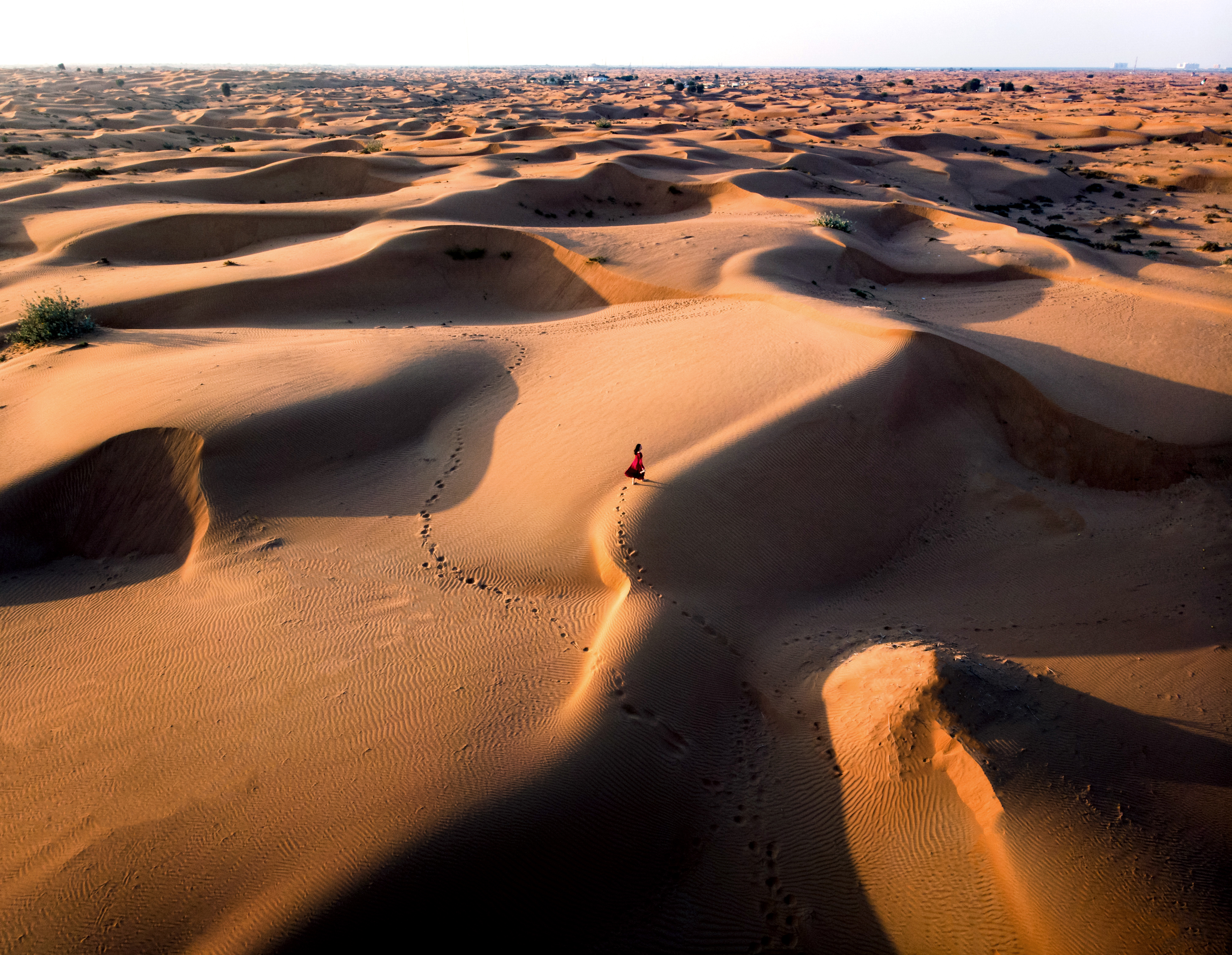 Person in red dress walking across golden desert dunes.