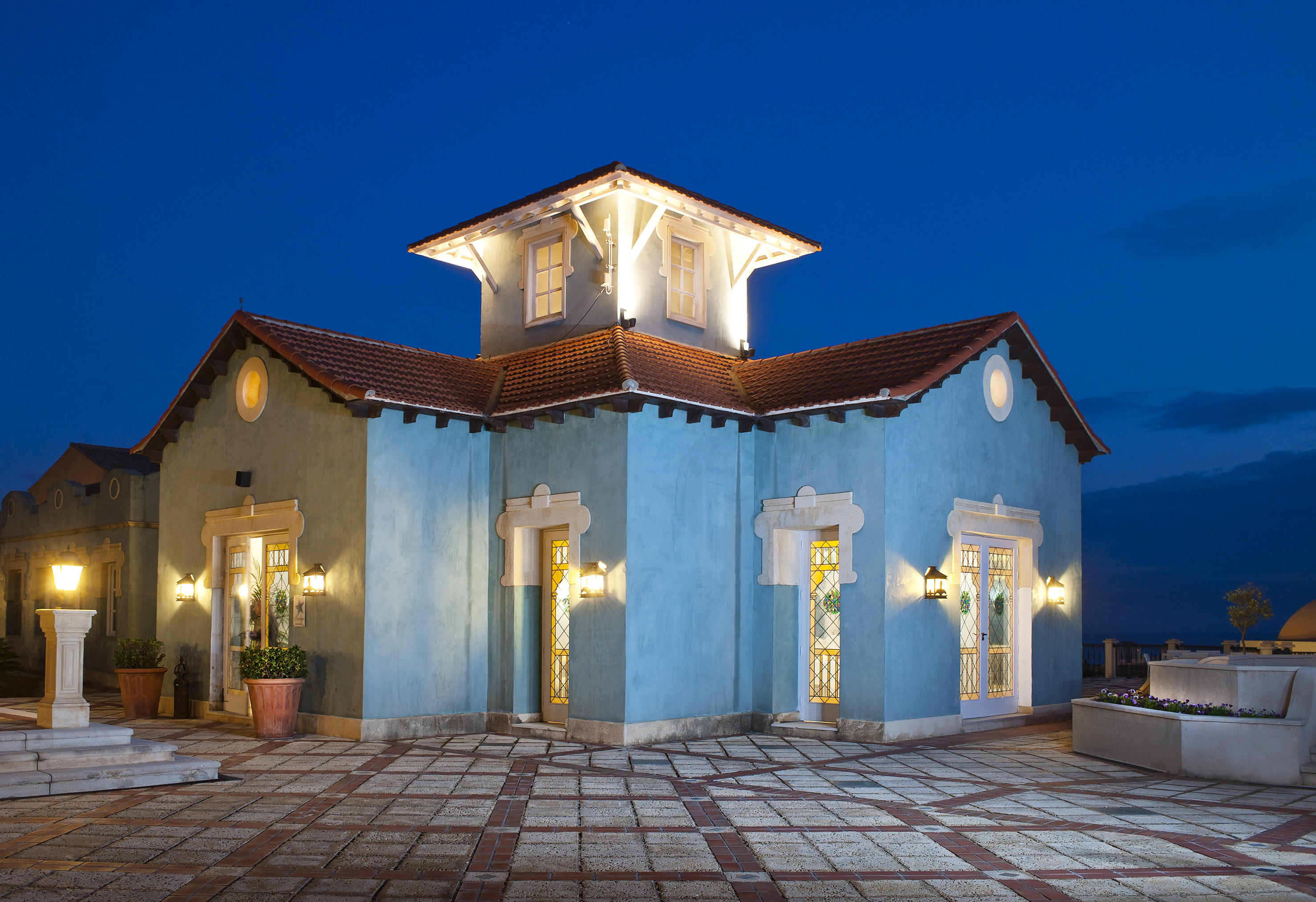 Mediterranean villa exterior, blue walls, red tile roof, illuminated at night.