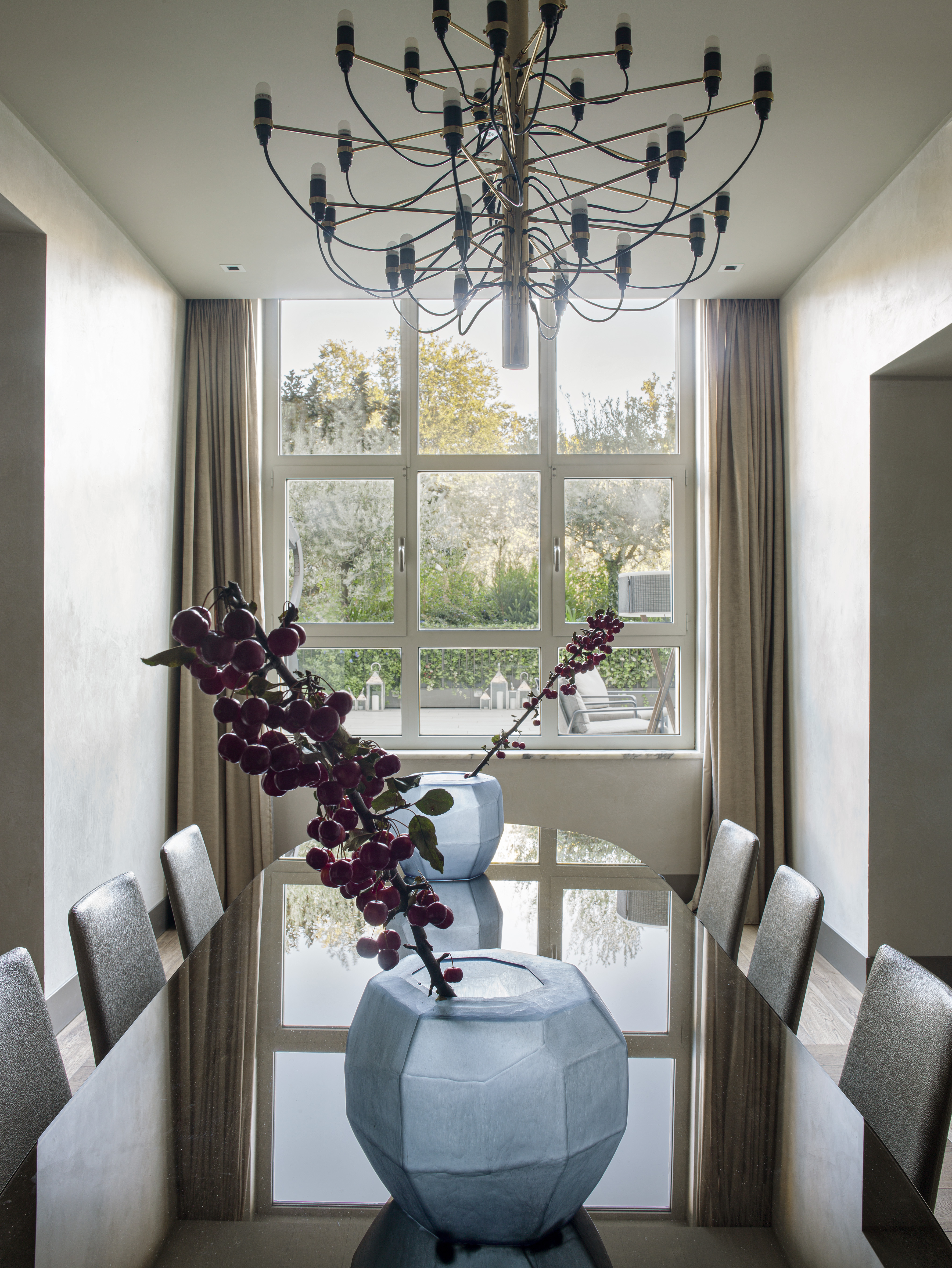 Modern dining room with long table, red berry decor, and brass chandelier.