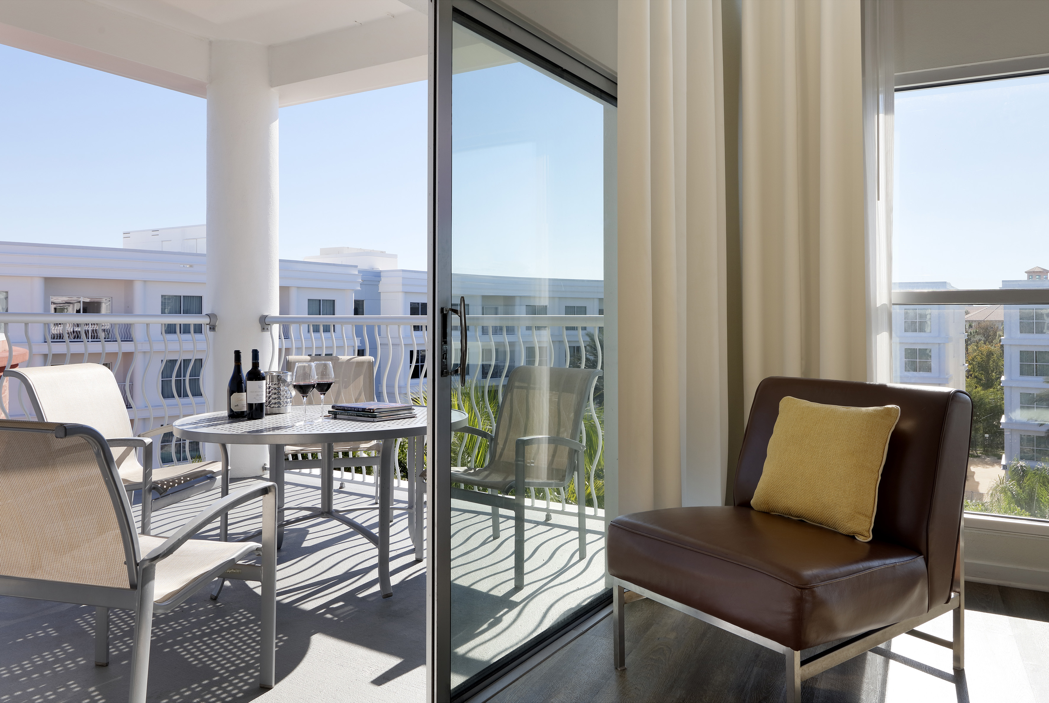 Balcony with outdoor table, wine, chairs, connected to indoor brown accent chair.