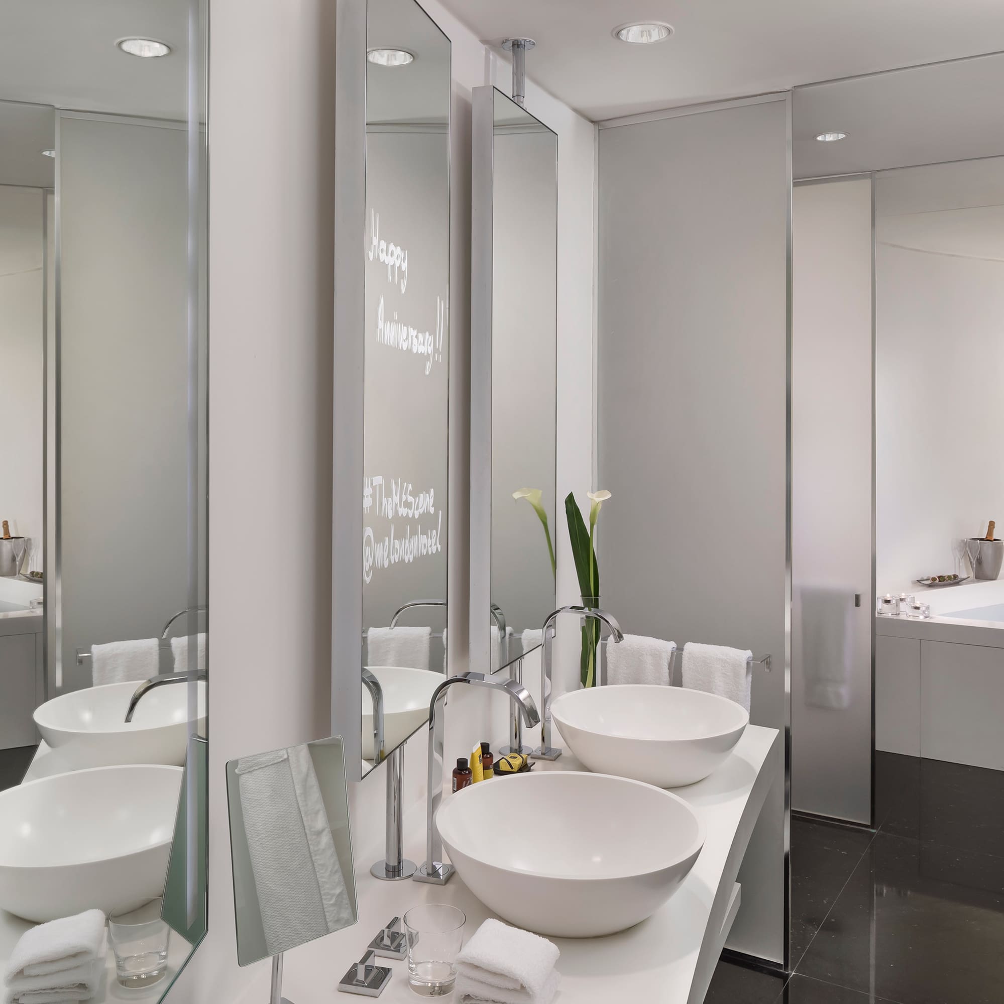 Modern hotel bathroom: dual sinks, tub, Happy Anniversary on mirror.