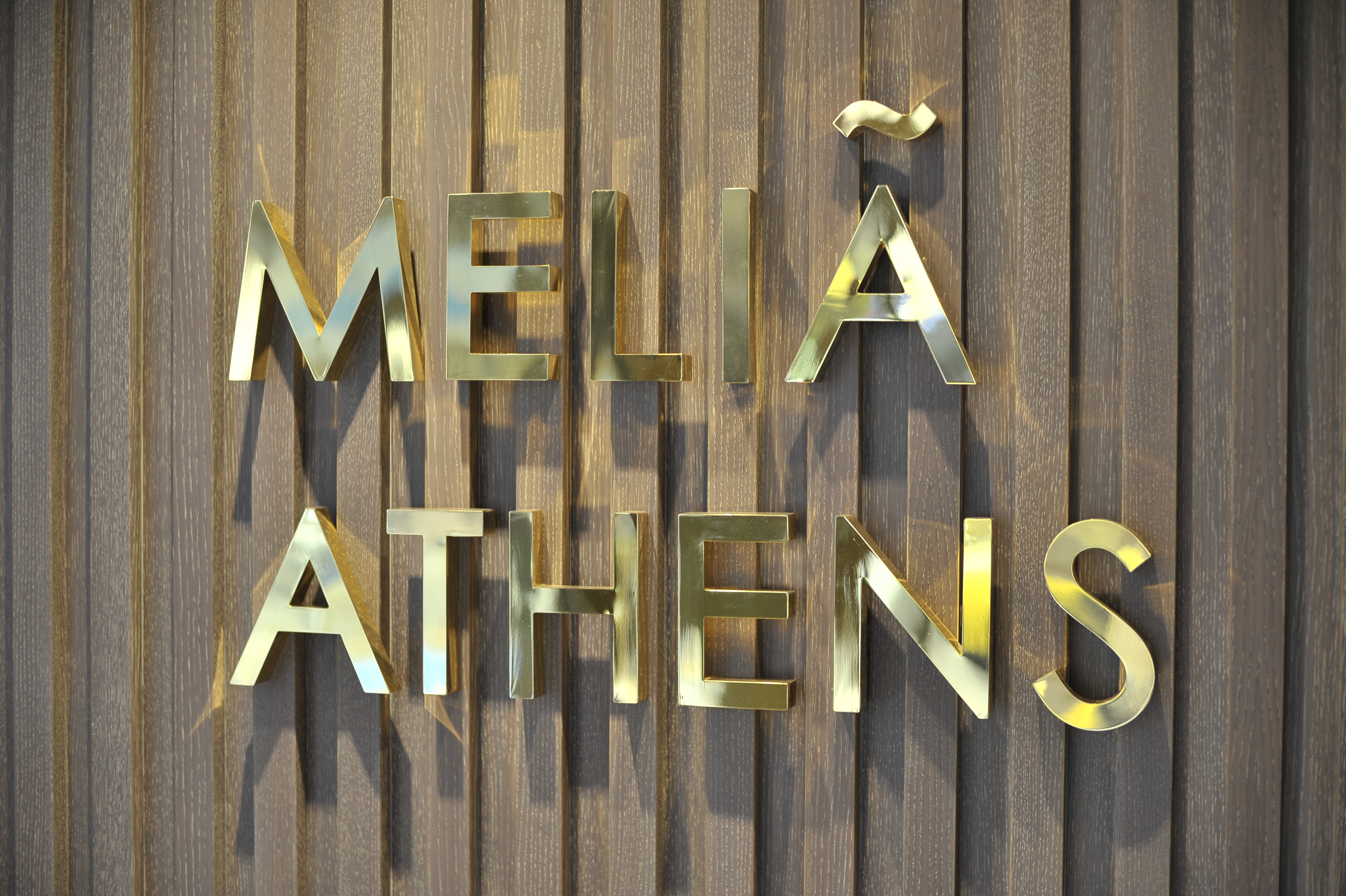 Meliã Athens hotel sign, golden letters on a dark wood panel wall.