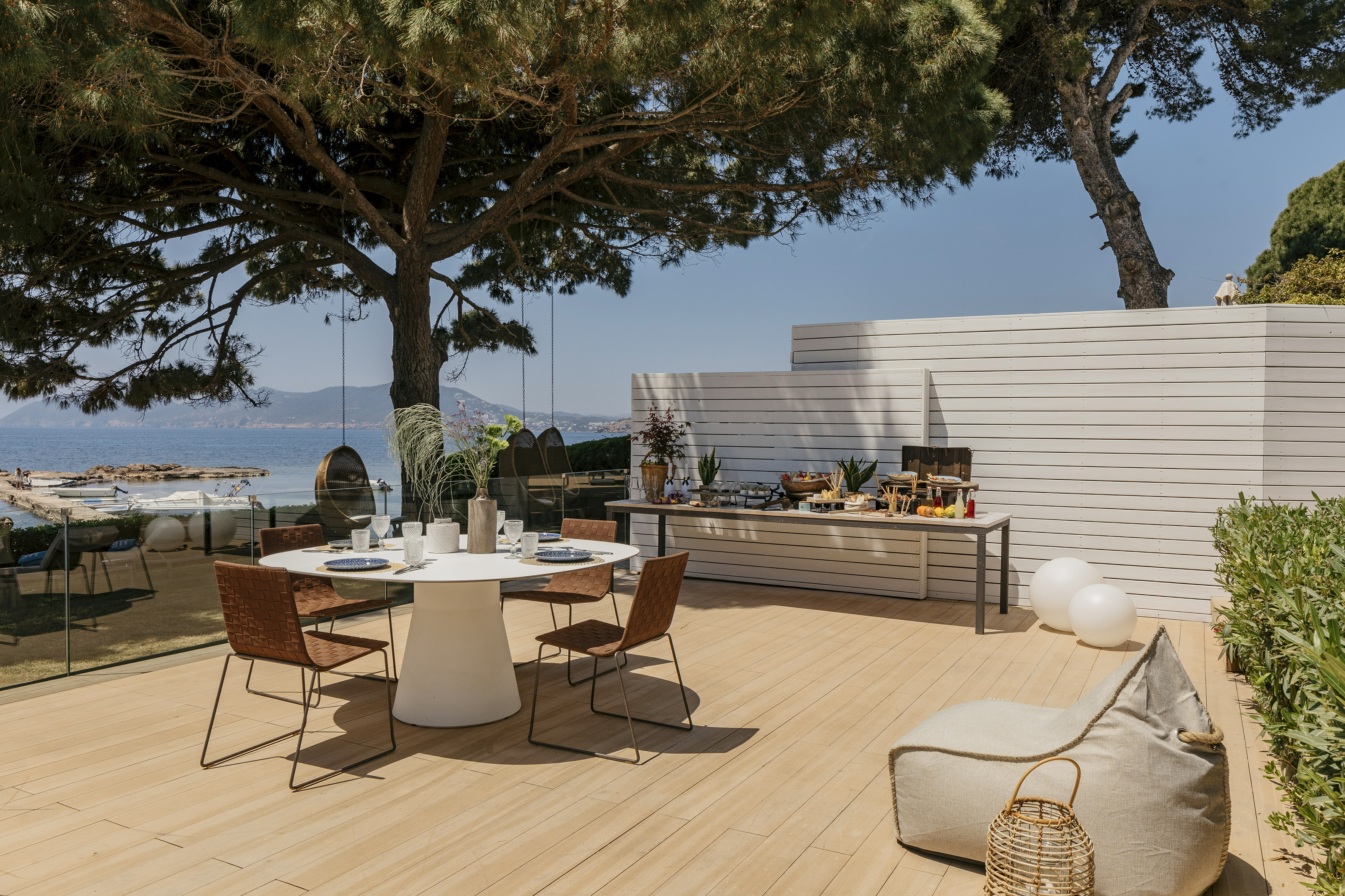 Coastal dining terrace with sea view, buffet, and shaded by a large tree.