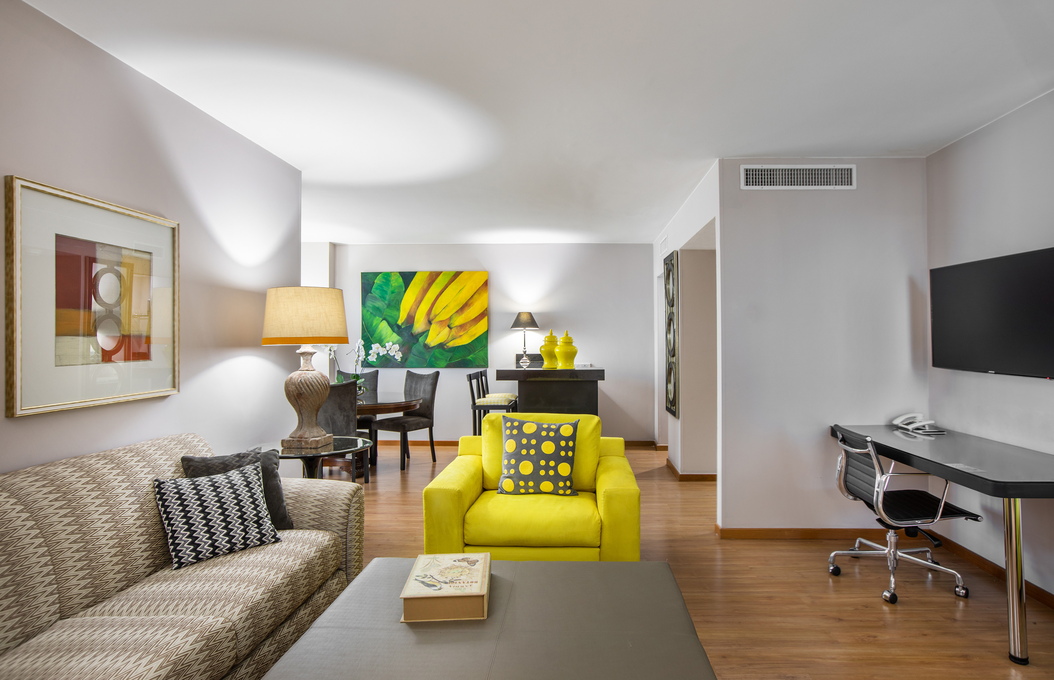 Living room with bright yellow armchair, patterned sofa, and banana art.