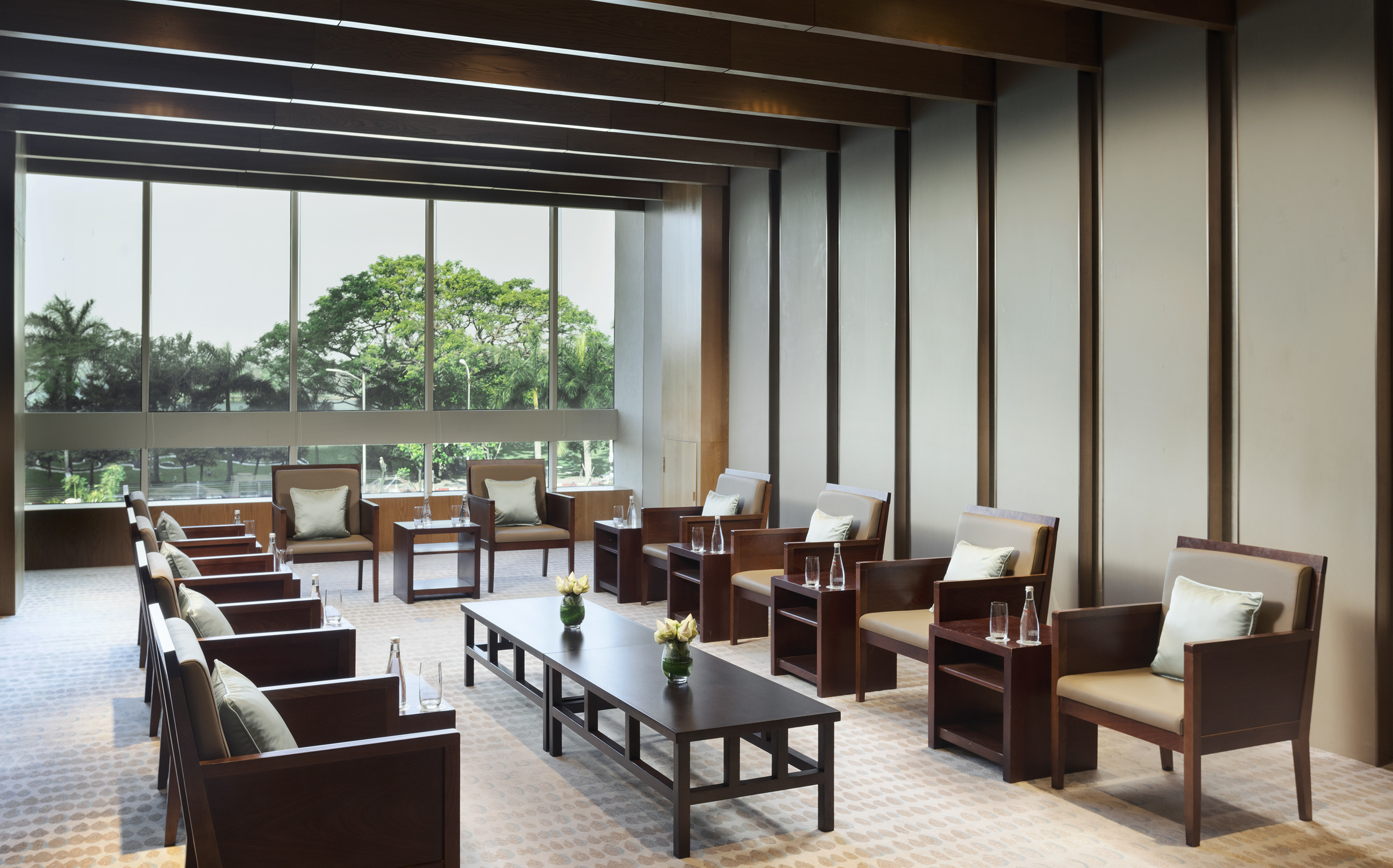 Executive lounge with modern seating, dark wood tables, and outdoor green view.