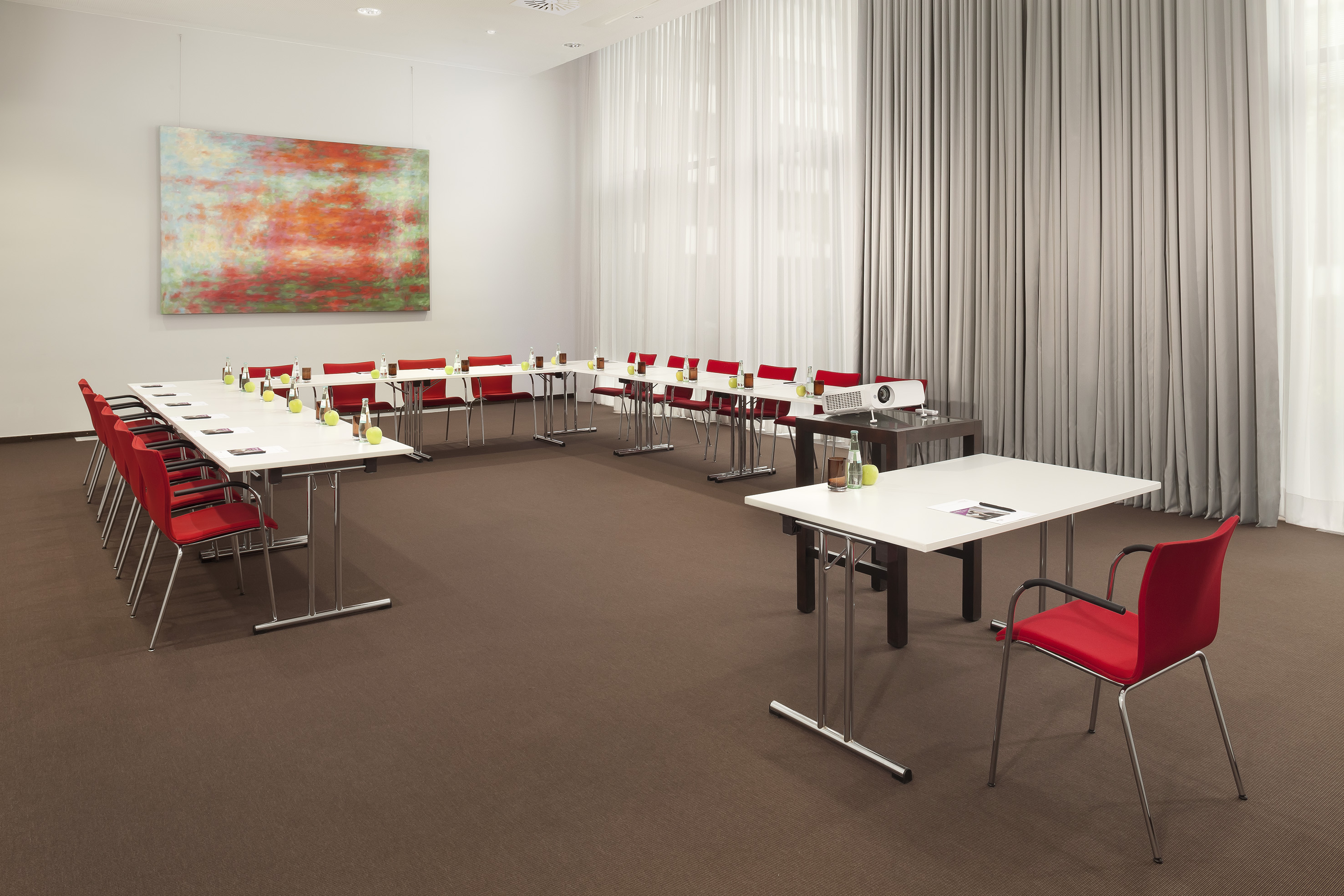 Modern conference room with white tables, red chairs, projector, abstract art.