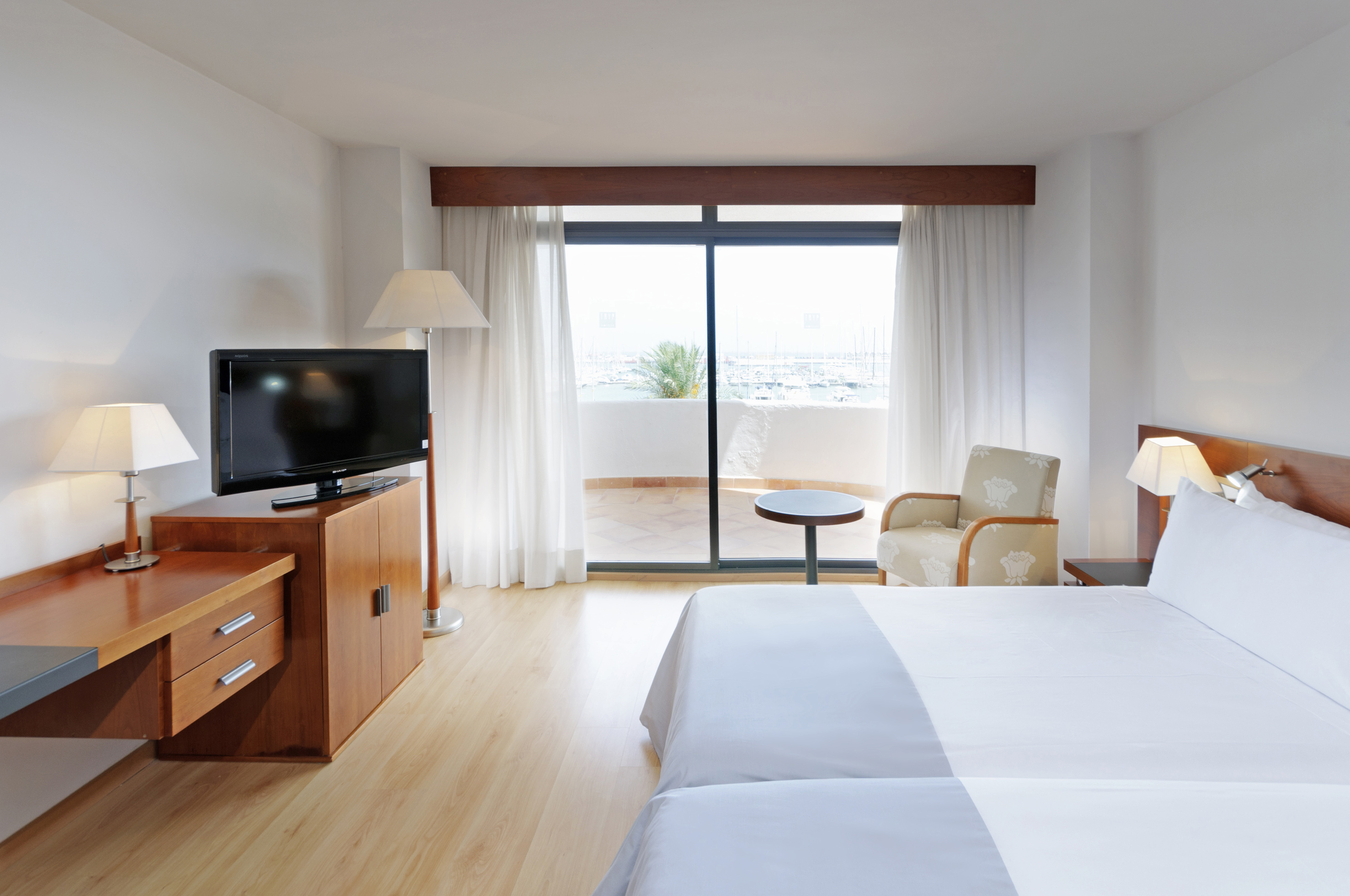 Modern hotel room with balcony, marina view, double bed, TV, and desk.