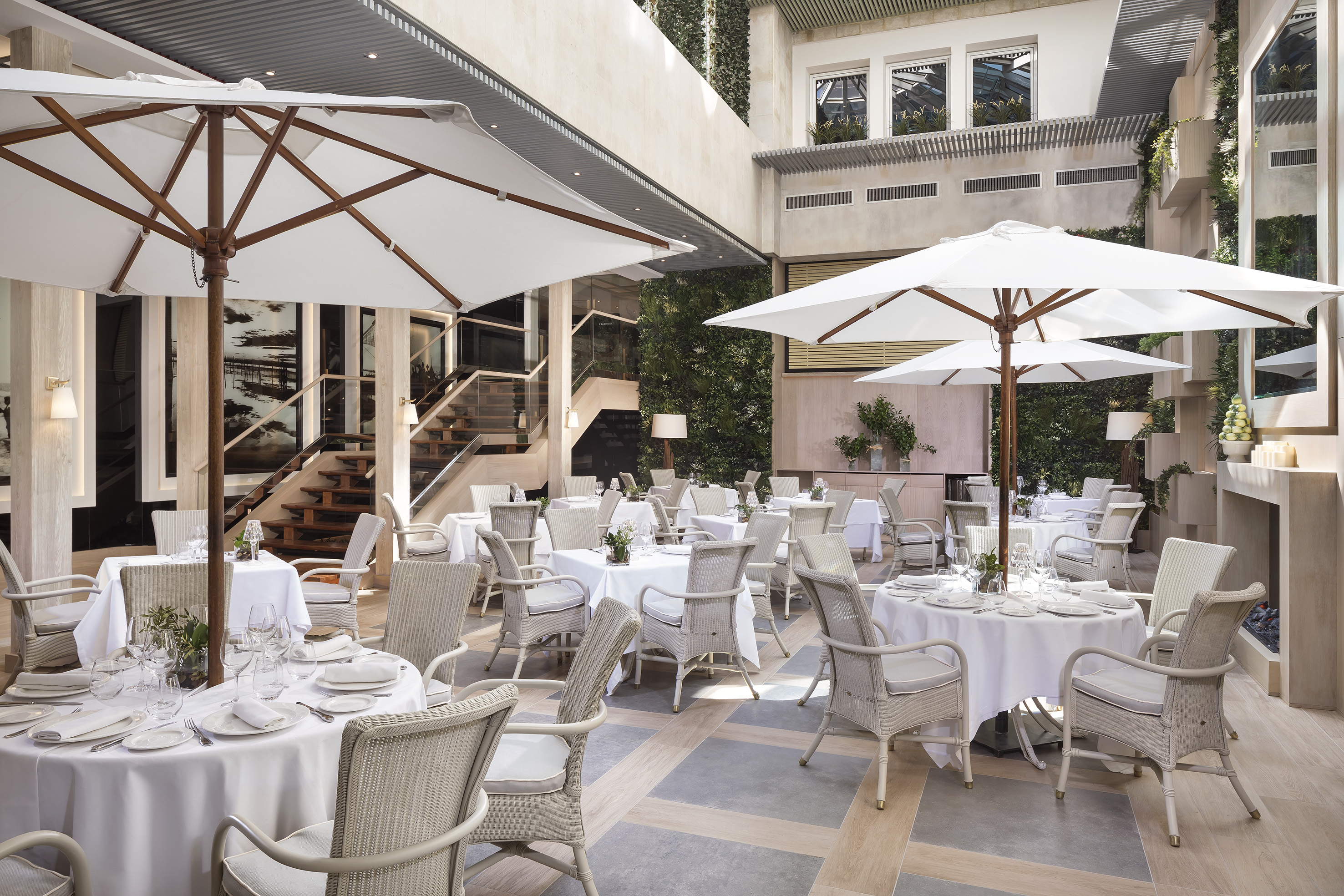 Upscale indoor-outdoor dining with white tables, wicker chairs, and patio umbrellas.