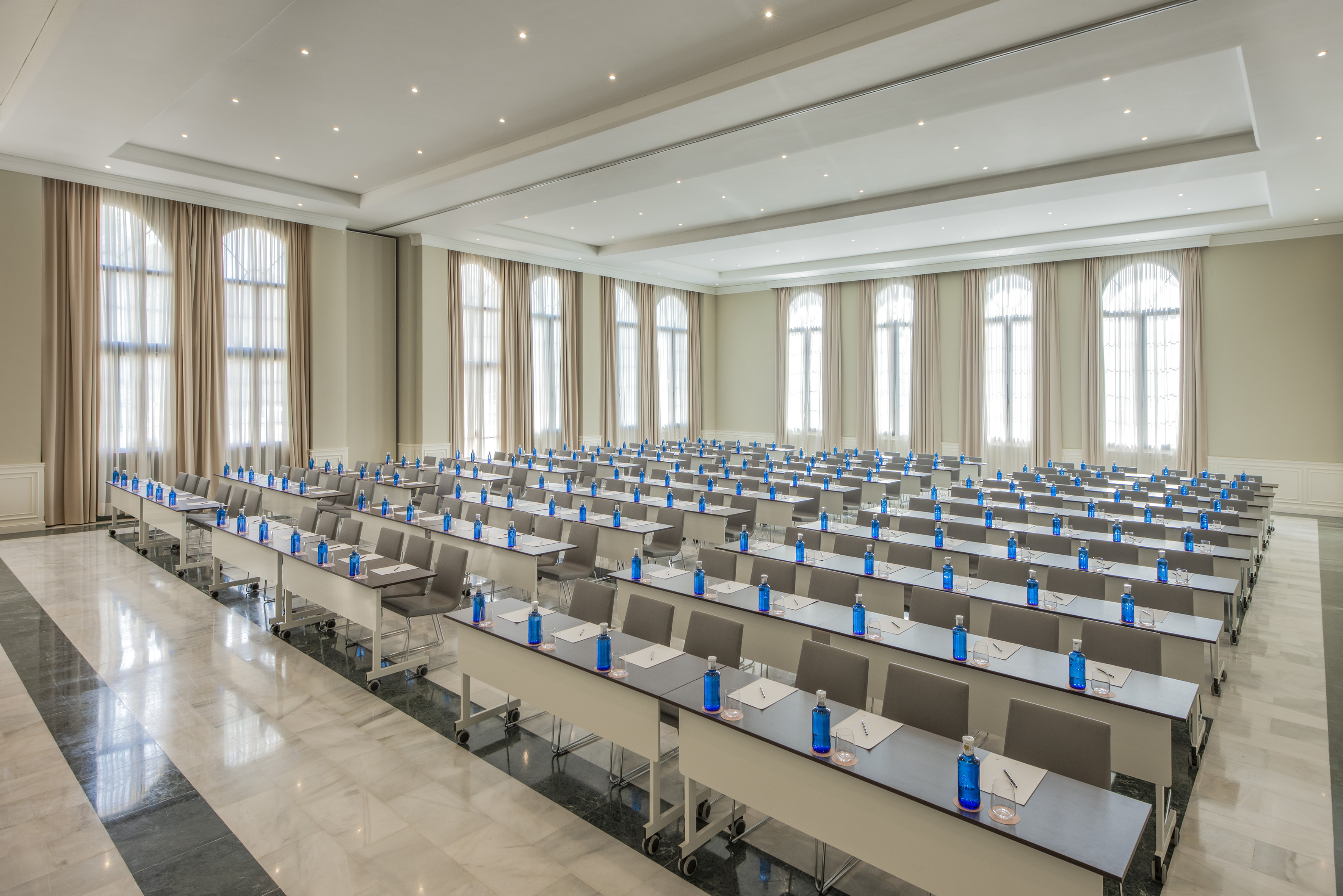 Empty hotel meeting room with rows of tables, chairs, and blue water bottles.
