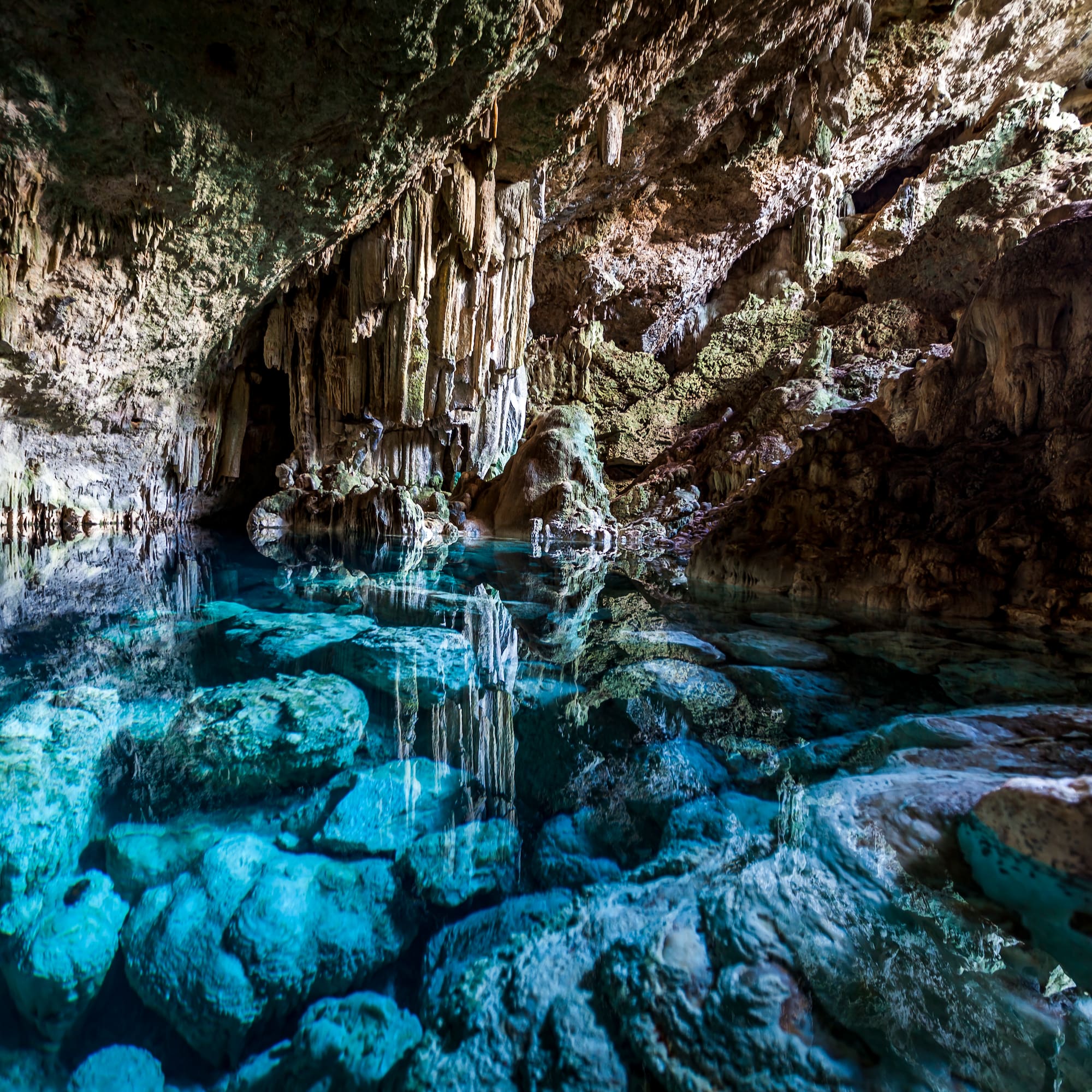 Turquoise water in a cenote cave with stalactites and clear reflections.