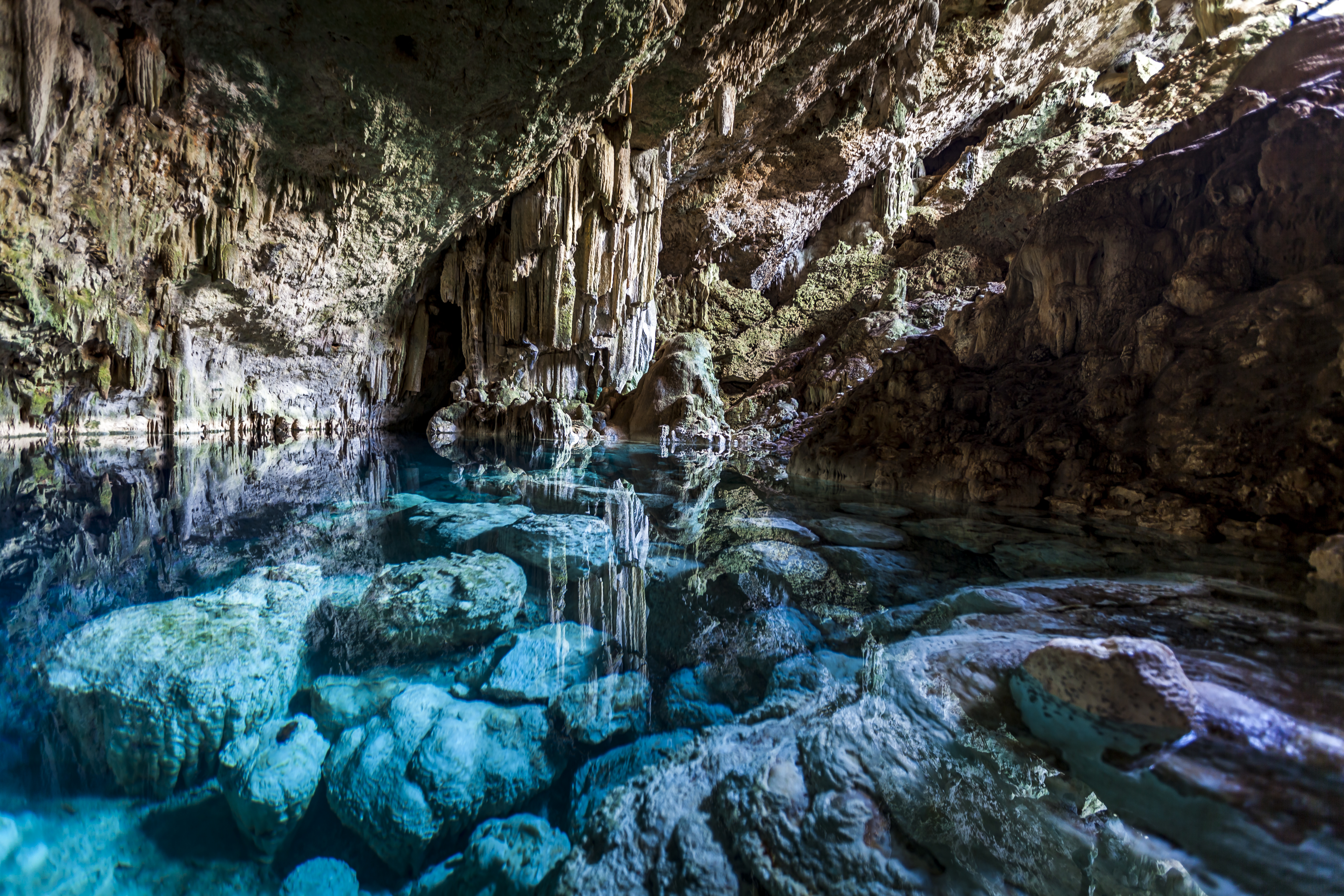 Turquoise water in a cenote cave with stalactites and clear reflections.