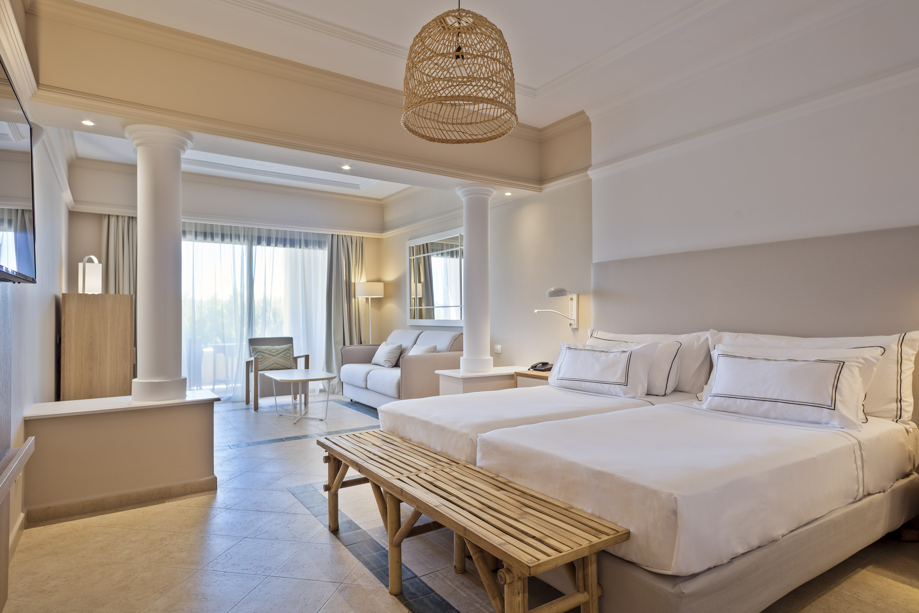 Modern hotel suite with neutral decor, two beds, and a separate living area.