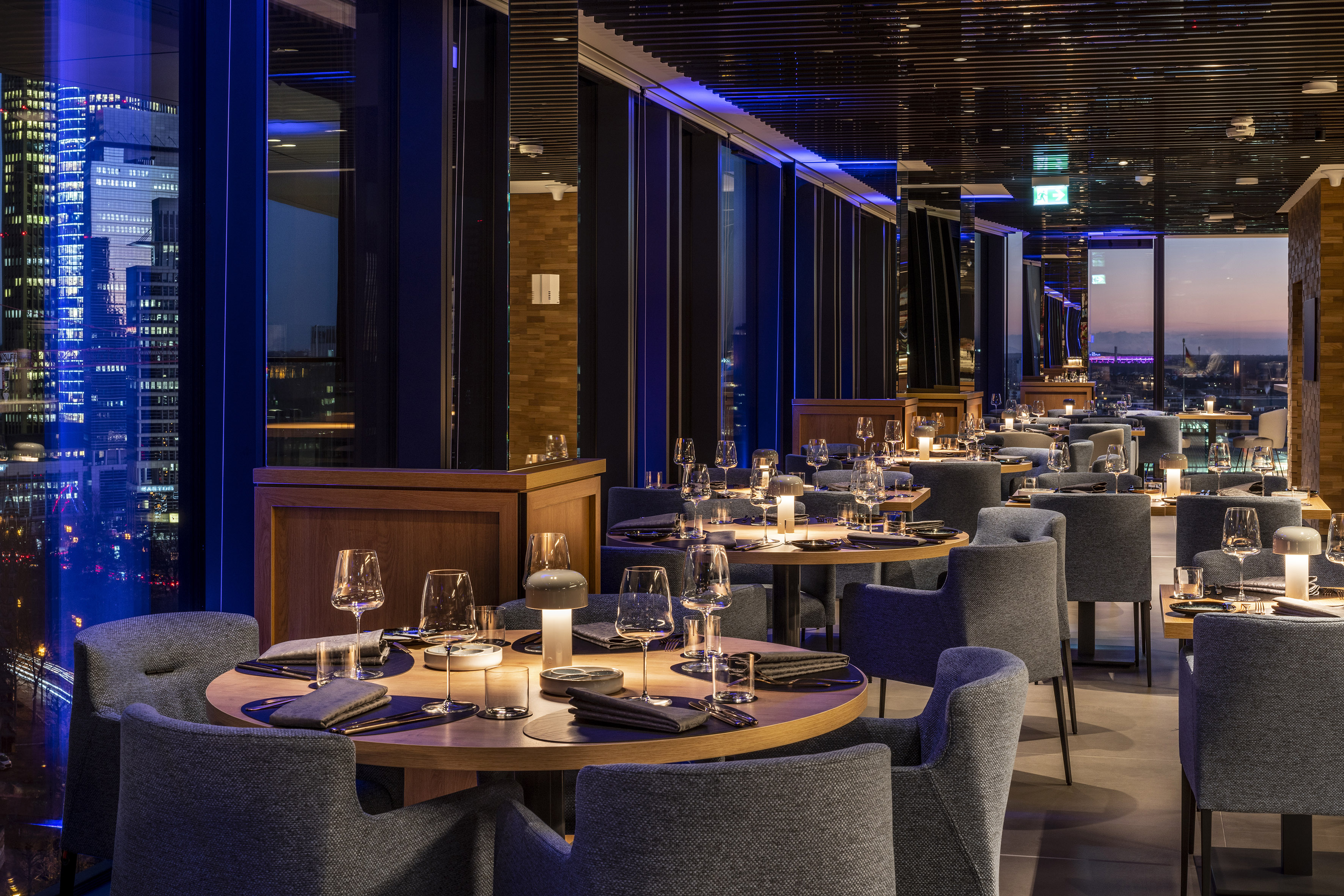 Elegant restaurant with night city view, set tables, and blue ambient lighting.