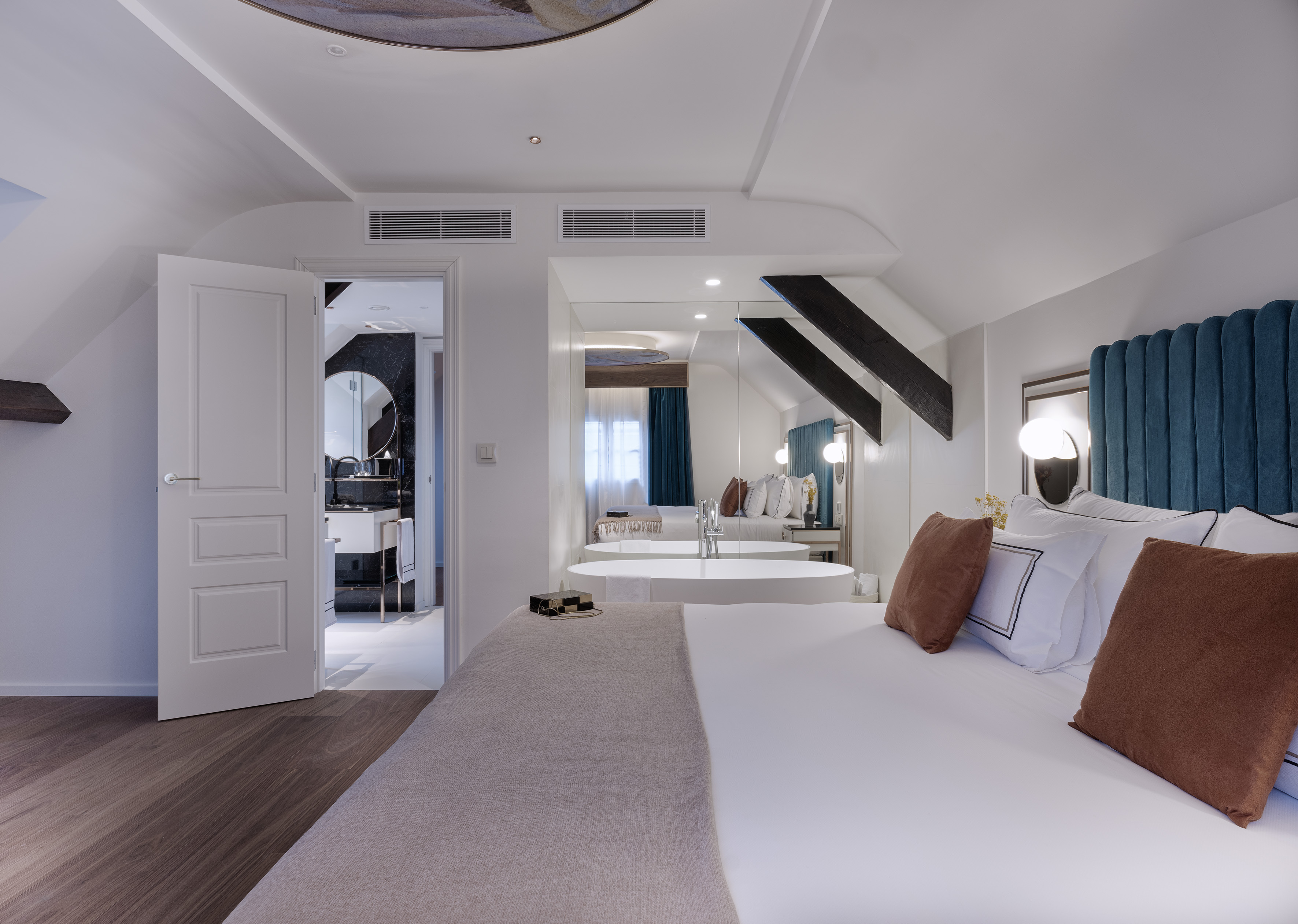 Modern hotel bedroom with king bed, freestanding tub, and elegant bathroom.
