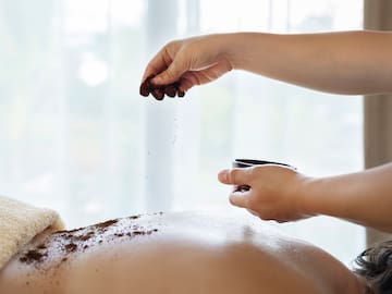 a person pouring brown powder on a person's back