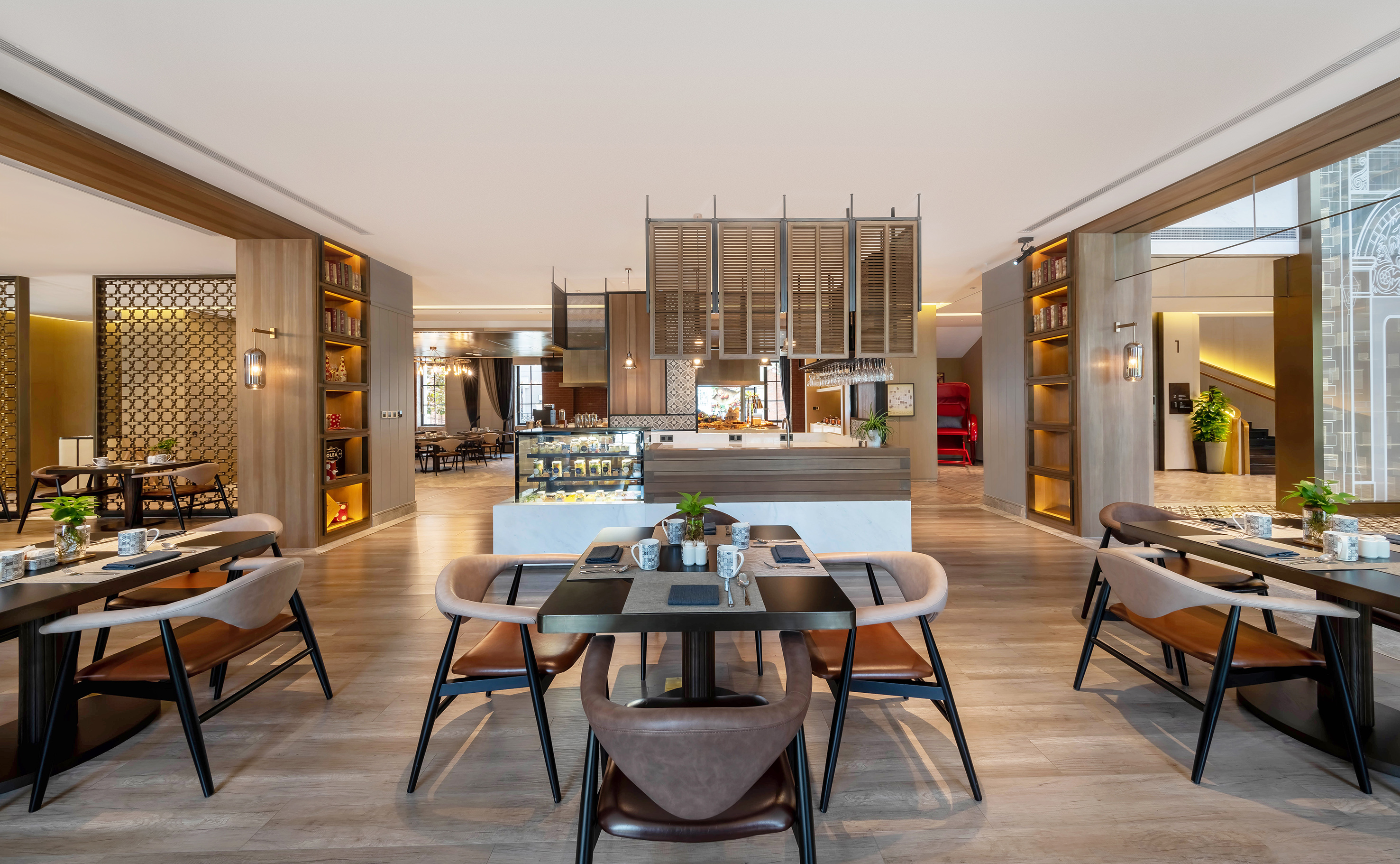 Modern hotel restaurant interior with dining tables, chairs, and pastry display.