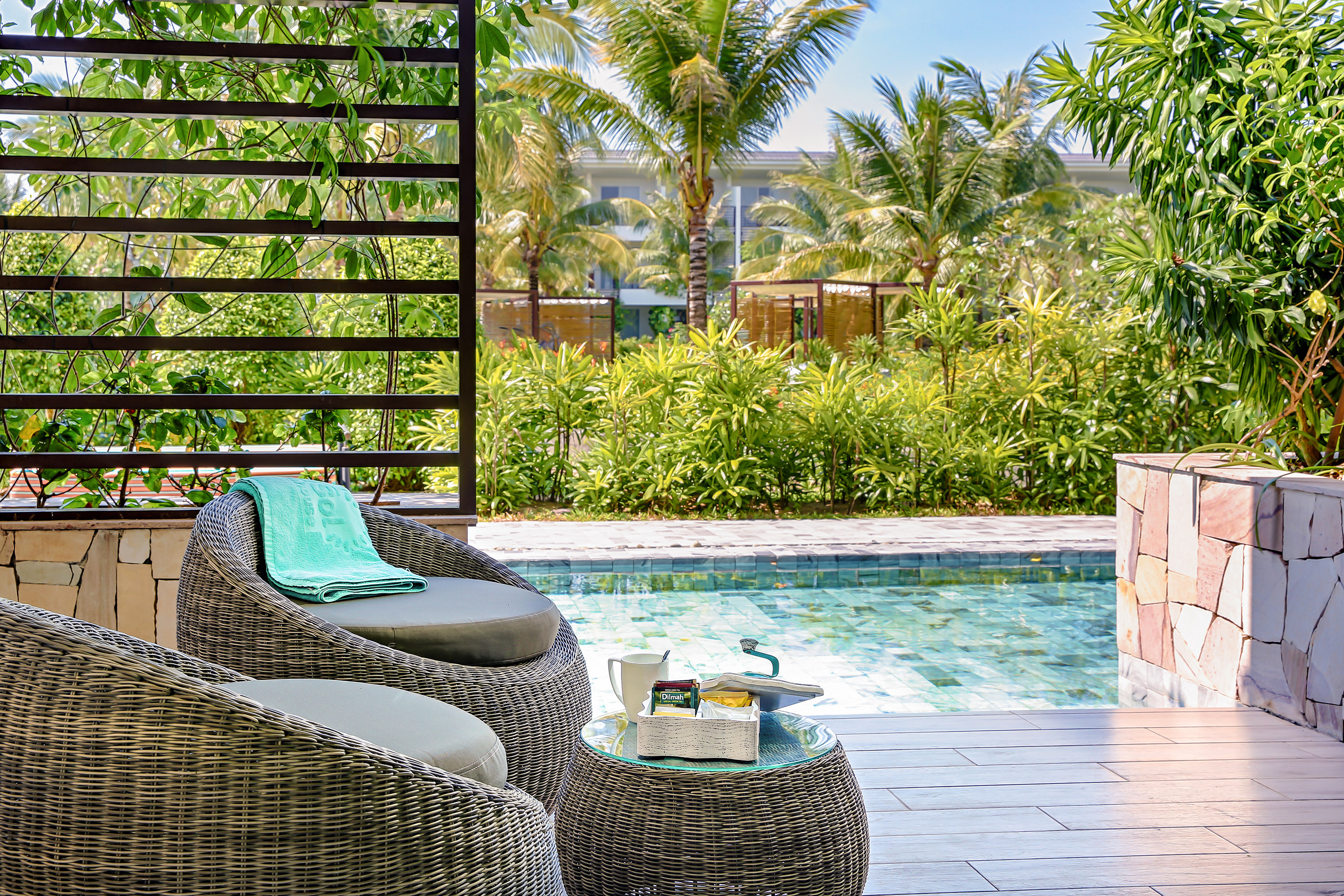 Tropical resort patio with wicker seating, pool, and lush greenery.
