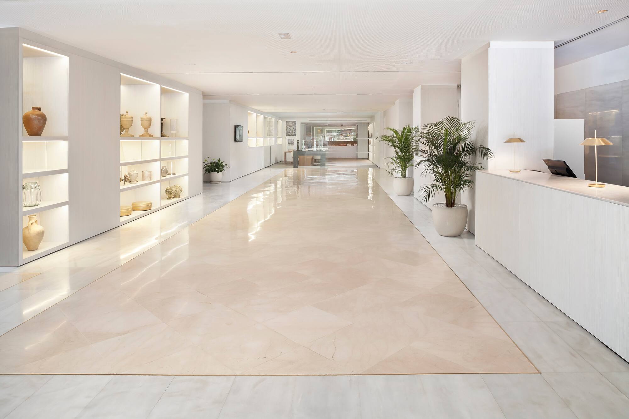 Bright hotel lobby with polished marble floor, illuminated shelves, and reception desk.