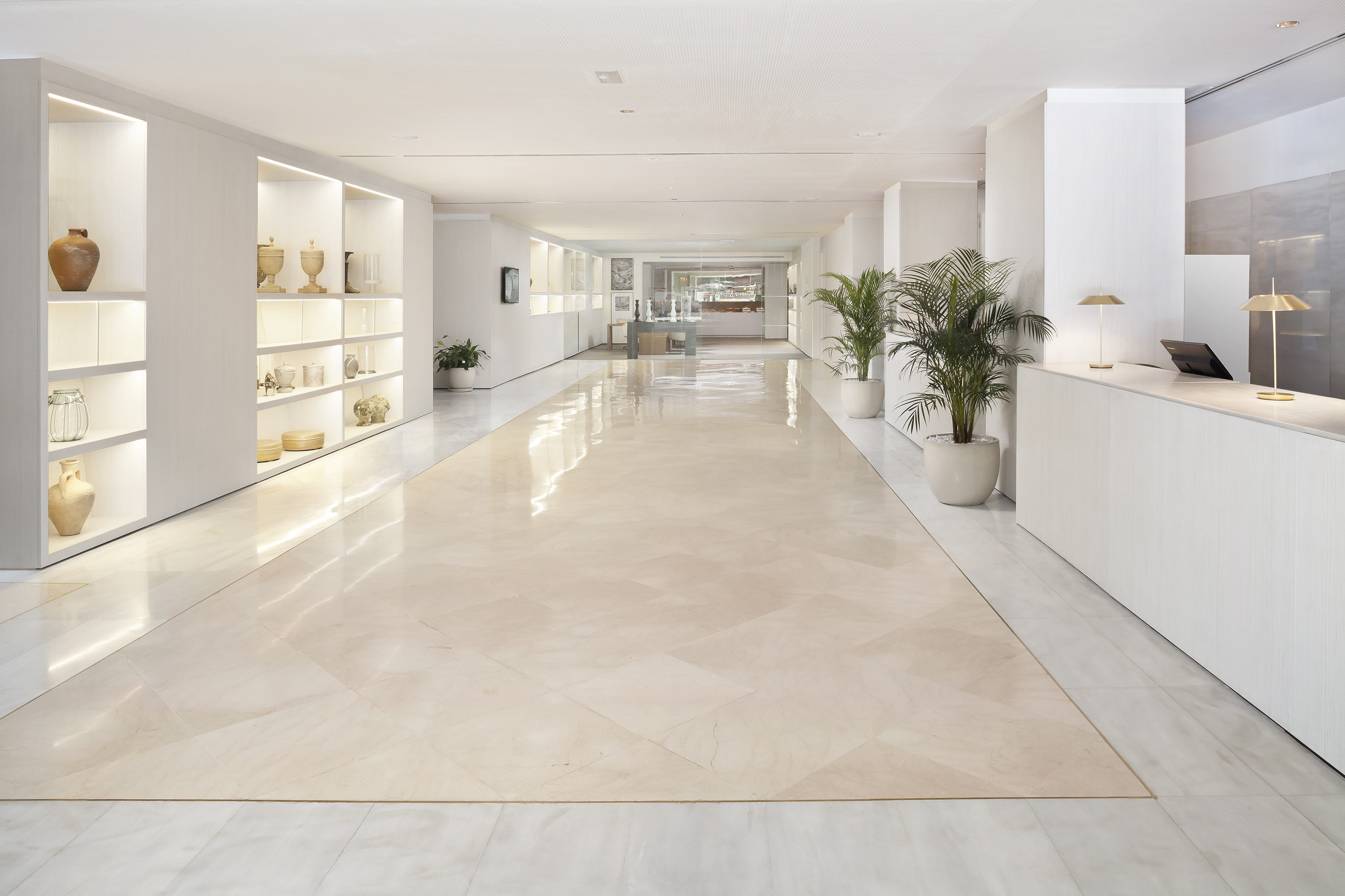 Bright hotel lobby with polished marble floor, illuminated shelves, and reception desk.