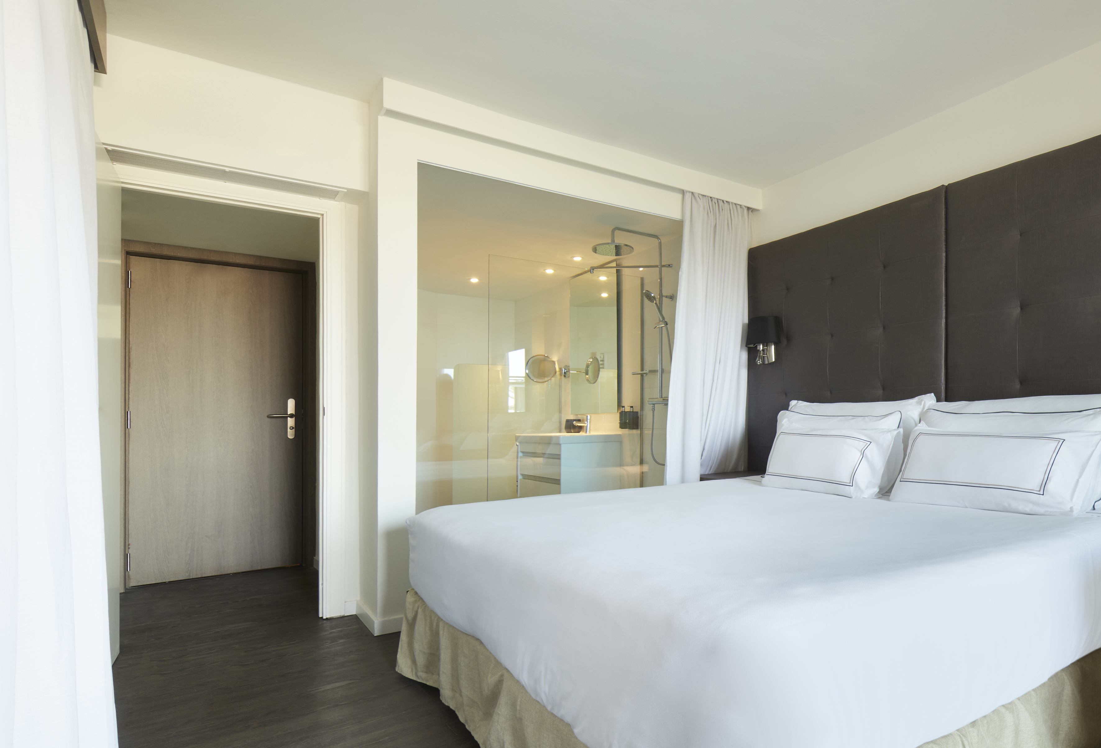 Modern hotel room with king bed, dark headboard, and glass bathroom.
