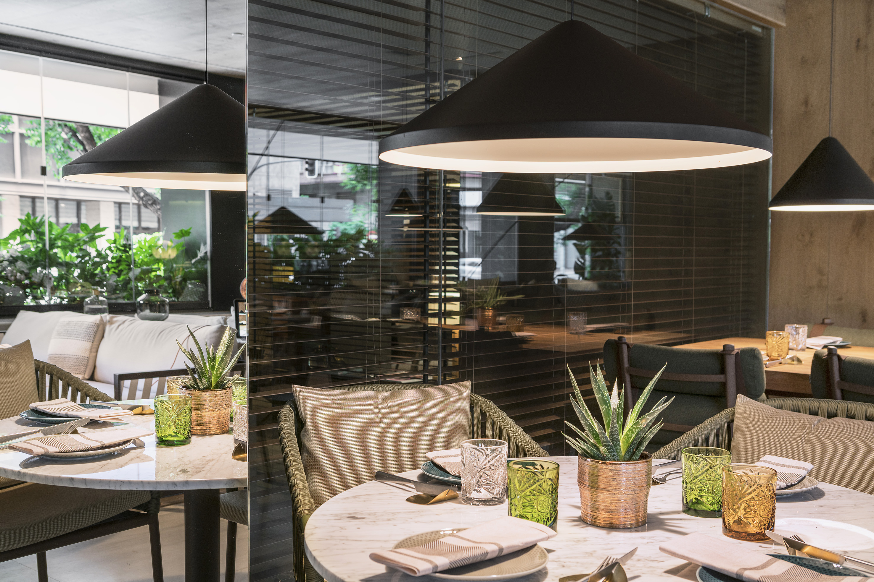 Modern restaurant interior with marble tables, conical pendant lights, and potted succulents.