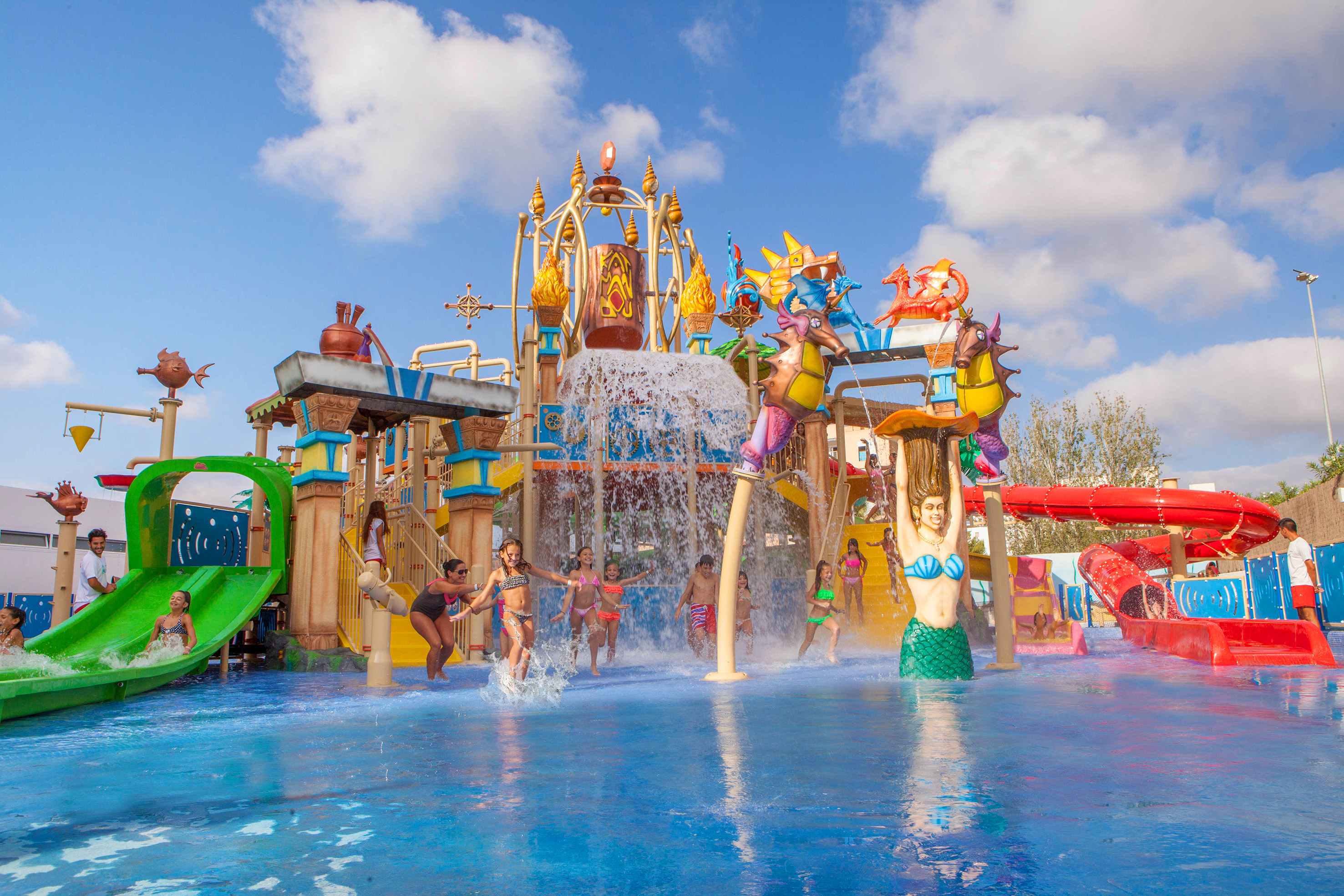 Kids playing at a vibrant water park with slides and a dumping bucket.