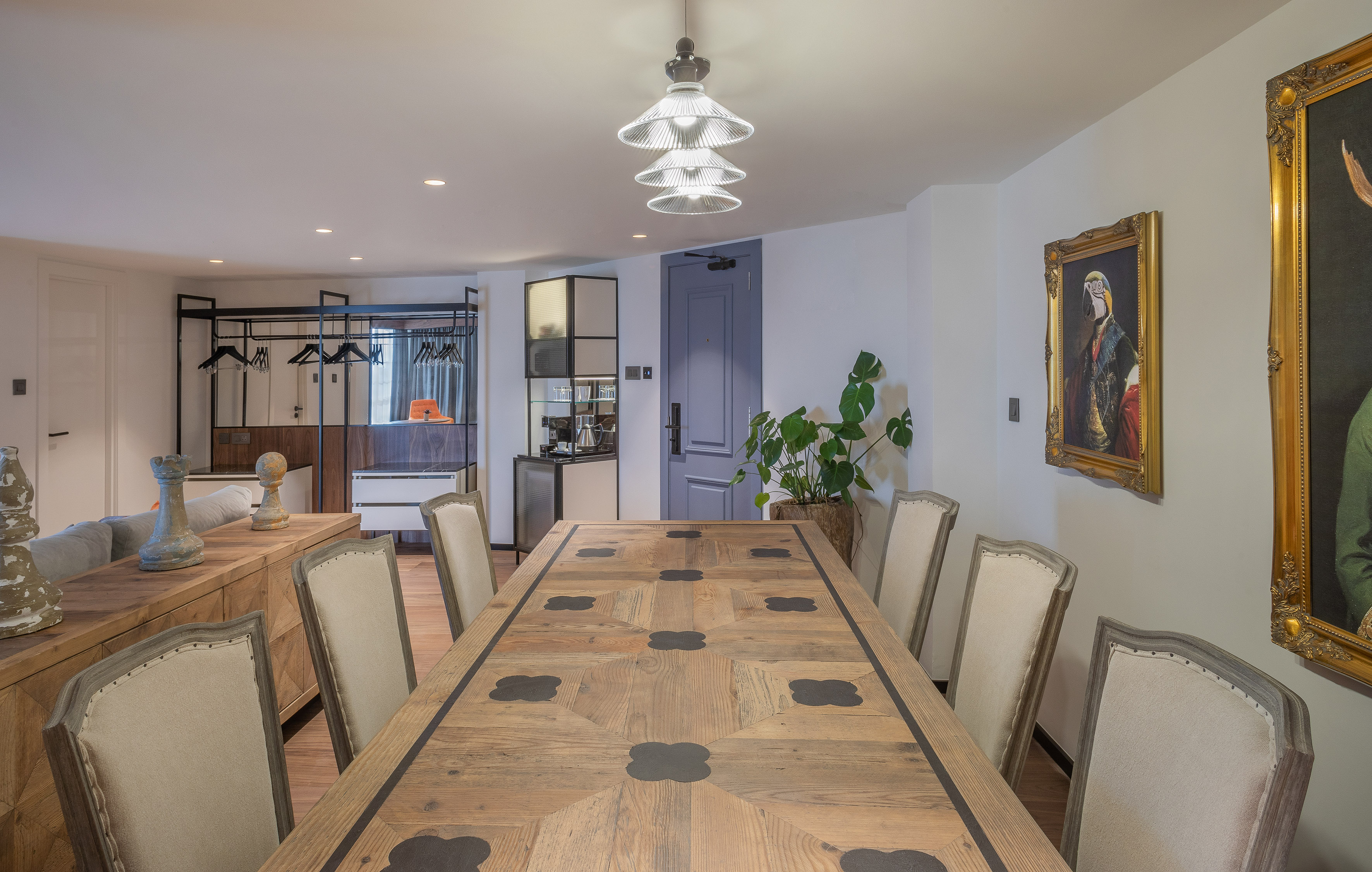 Modern hotel suite dining room with large wooden table, chairs, and tiered chandelier.