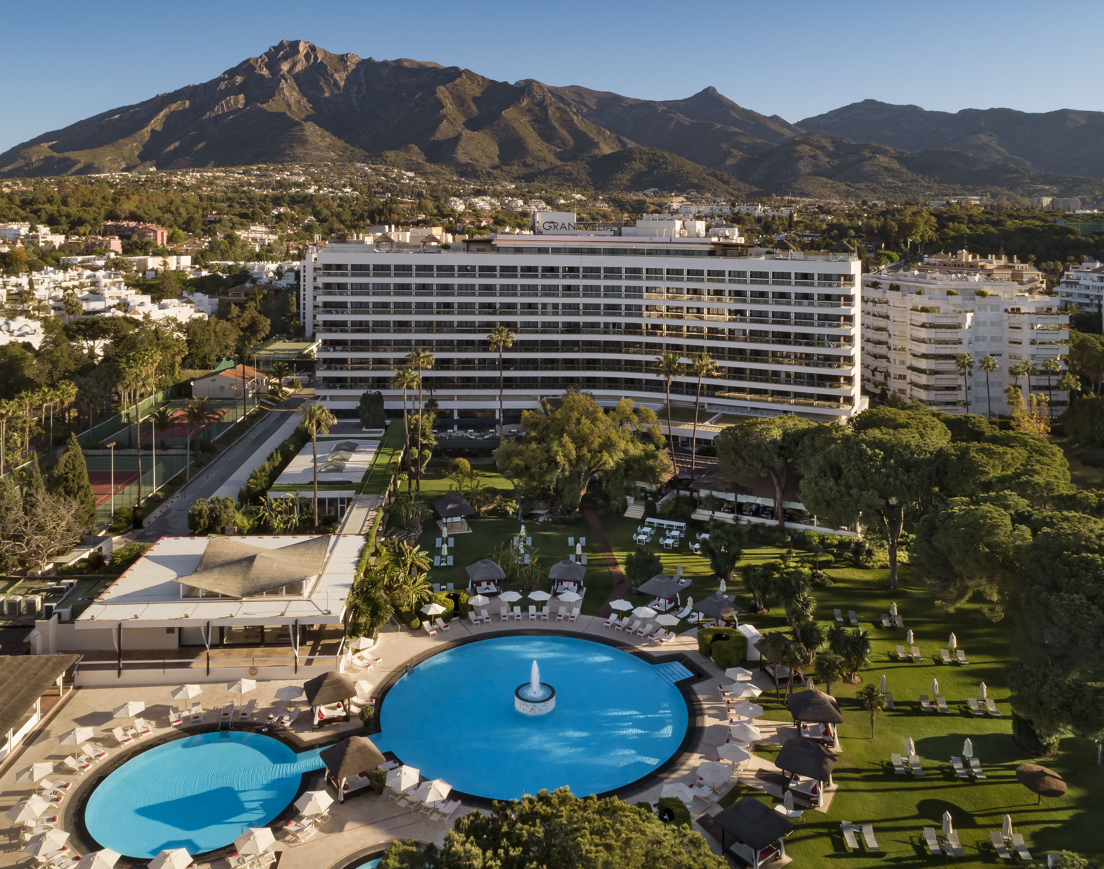 a pool in a resort with a large building and mountains in the background
