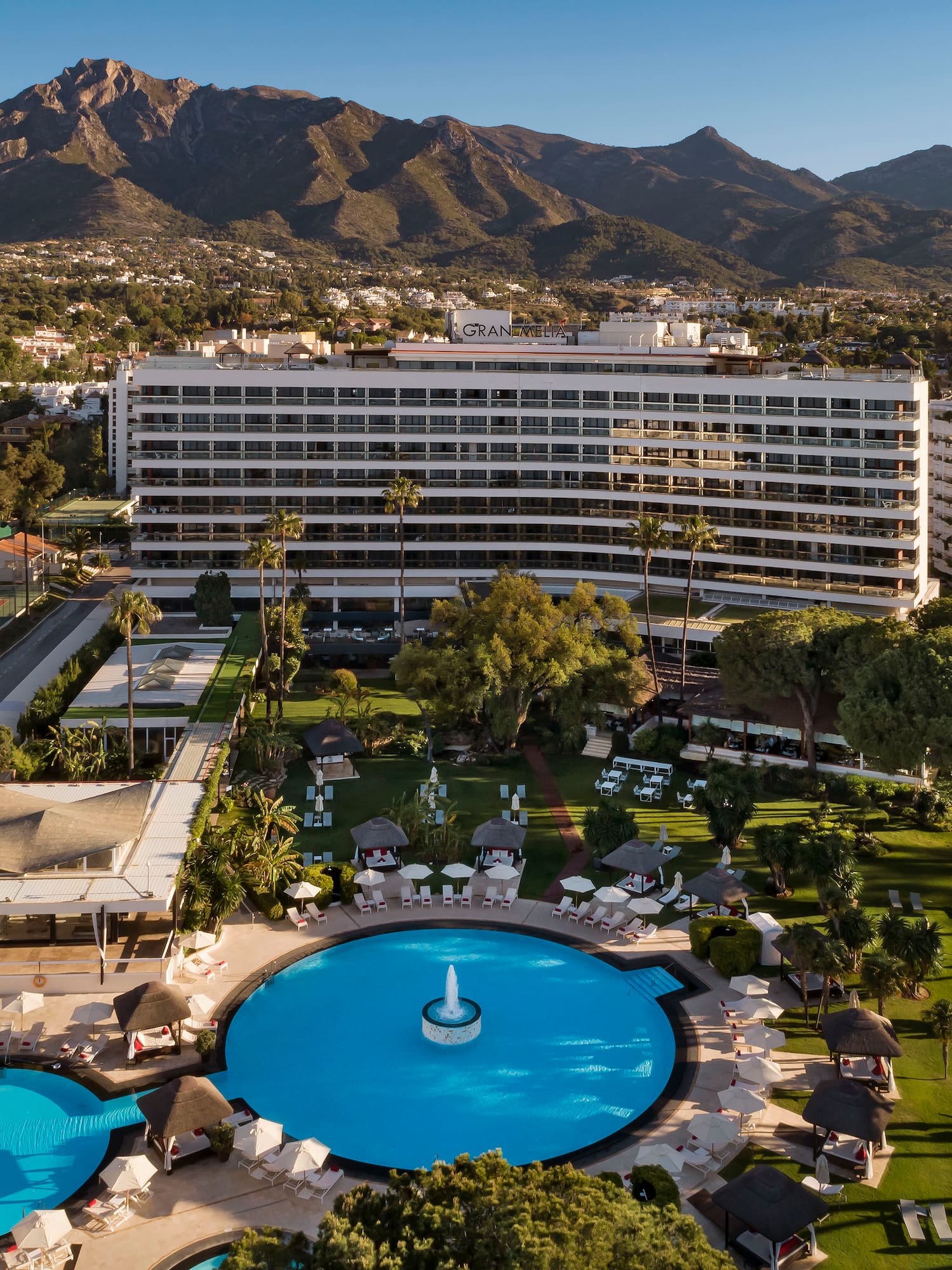 a pool in a resort with a large building and mountains in the background