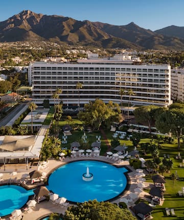 a pool in a resort with a large building and mountains in the background