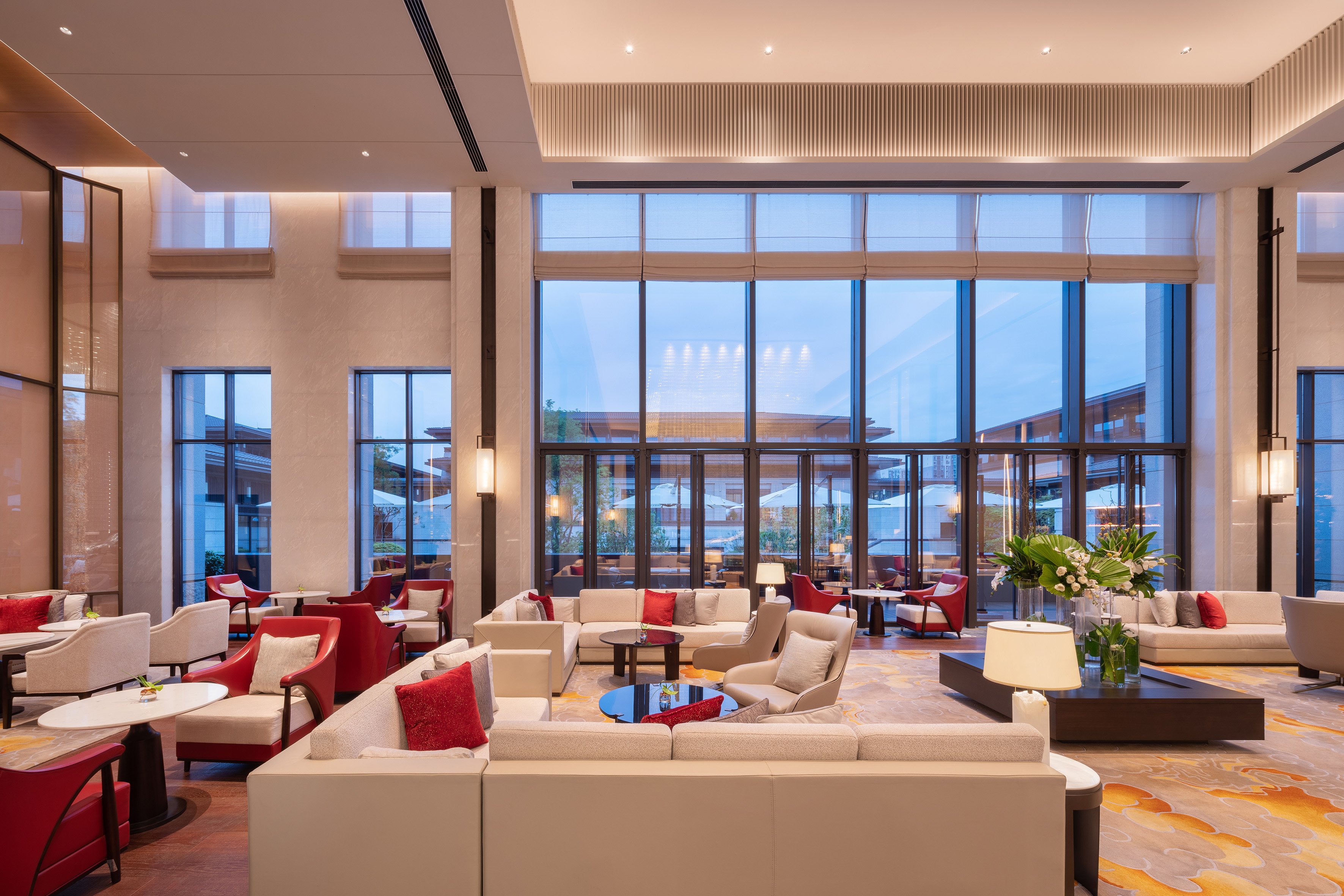 Luxury hotel lobby lounge with red & beige seating and large glass windows.
