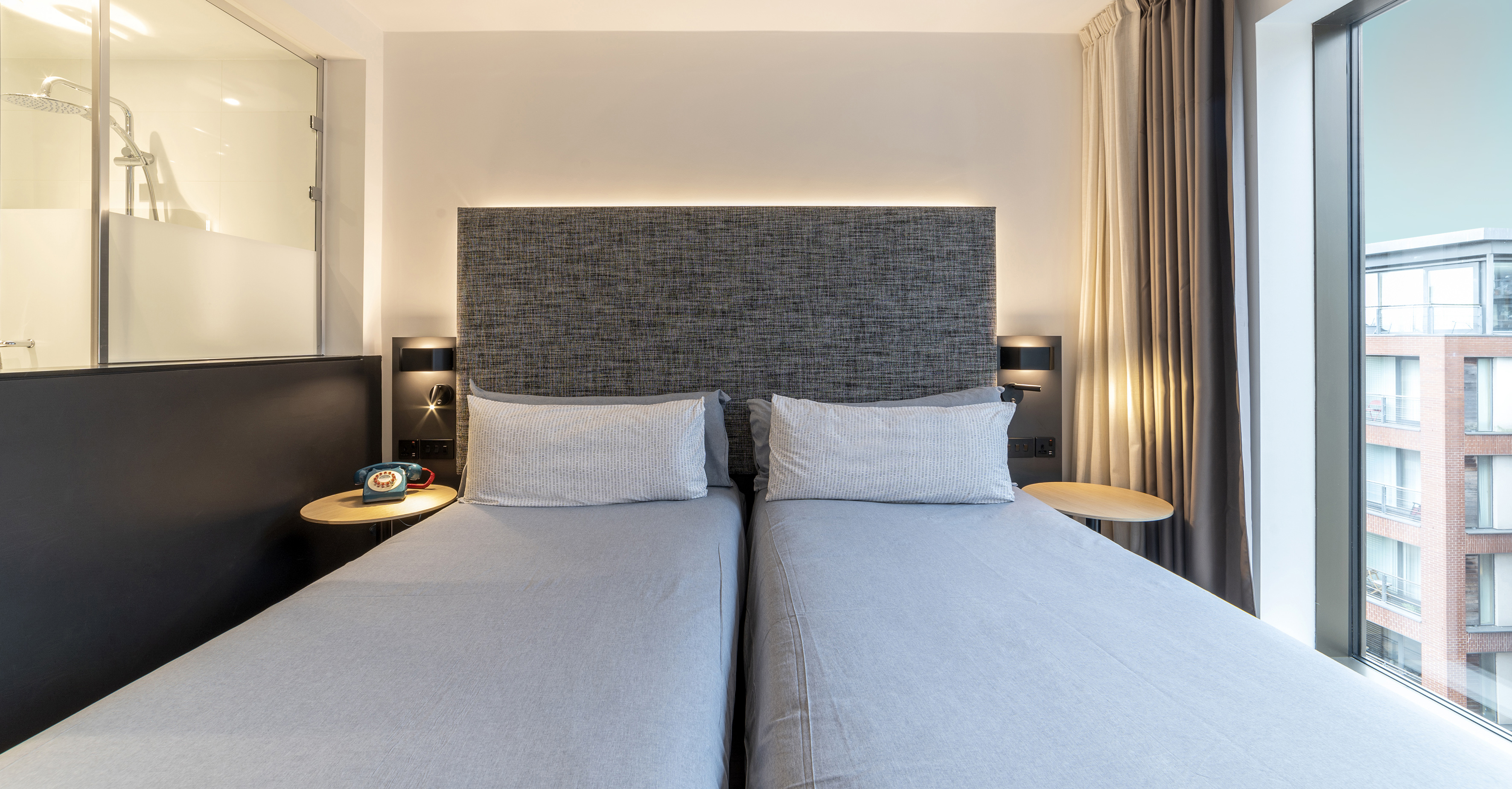 Modern hotel twin room with grey beds, city view, and ensuite shower.