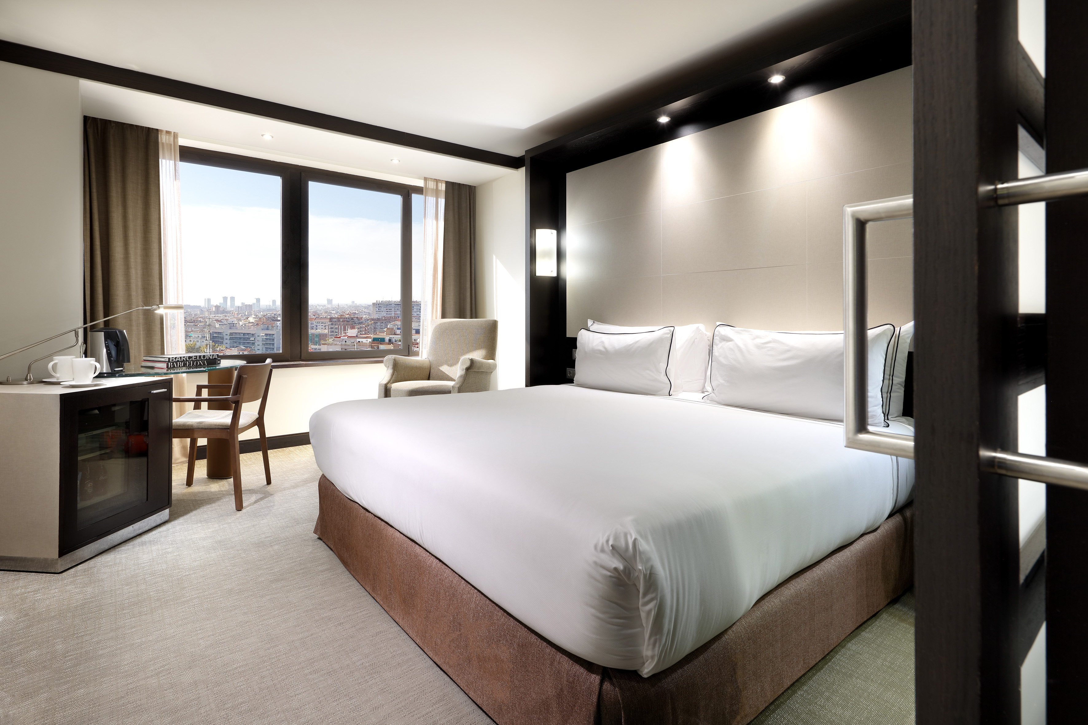 Luxury hotel room with large bed, city view, desk, and modern decor.
