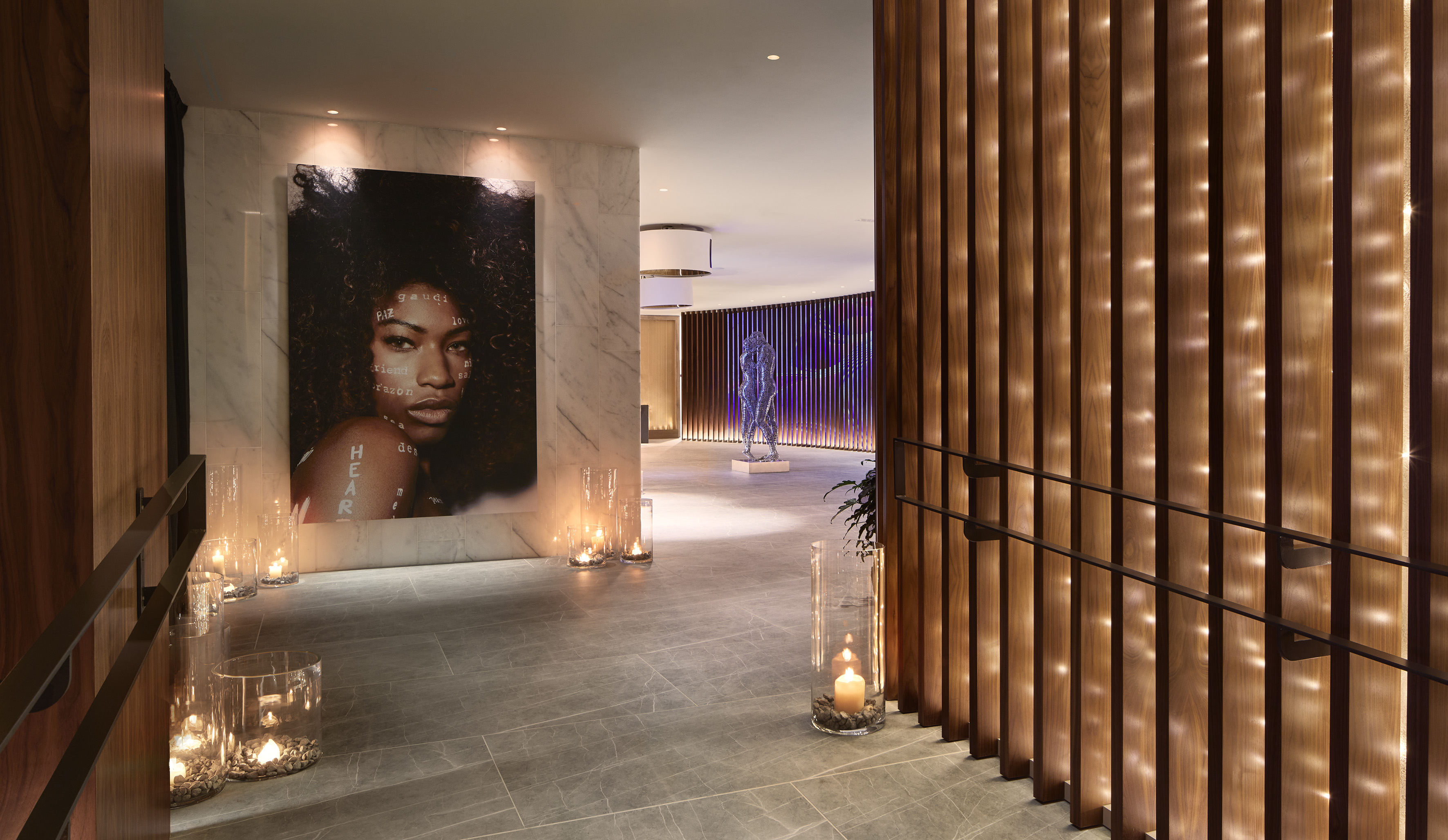Modern hallway with portrait art, wood slats, sculpture, and ambient candles.