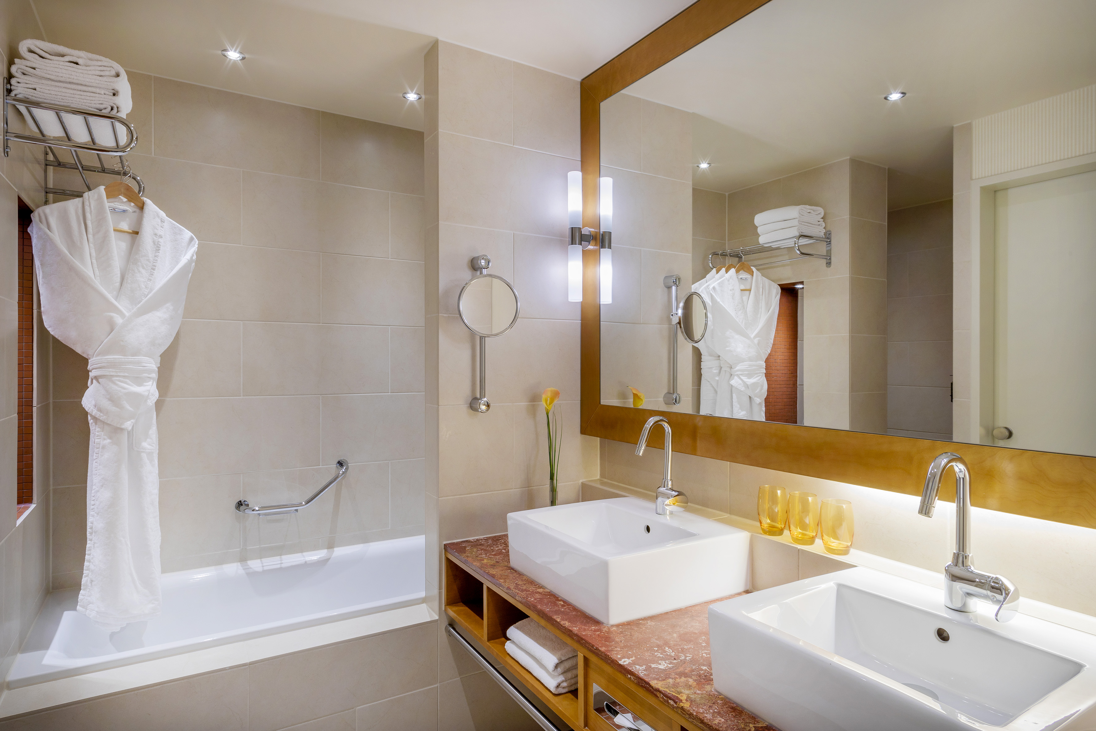 Hotel bathroom with double sinks, bathtub, large mirror, and white bathrobe.