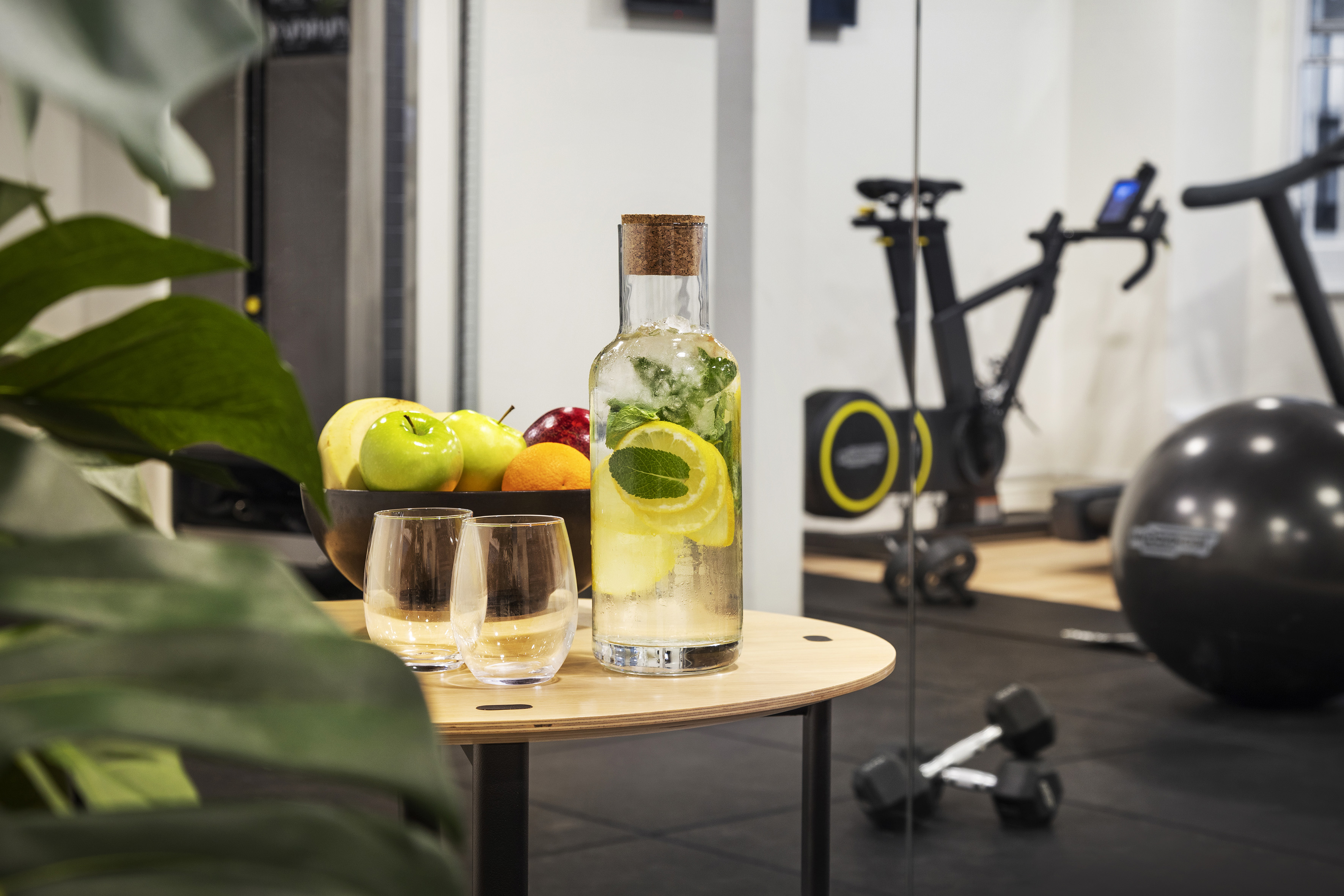 Lemon mint water, fresh fruit, and glasses on a gym table.
