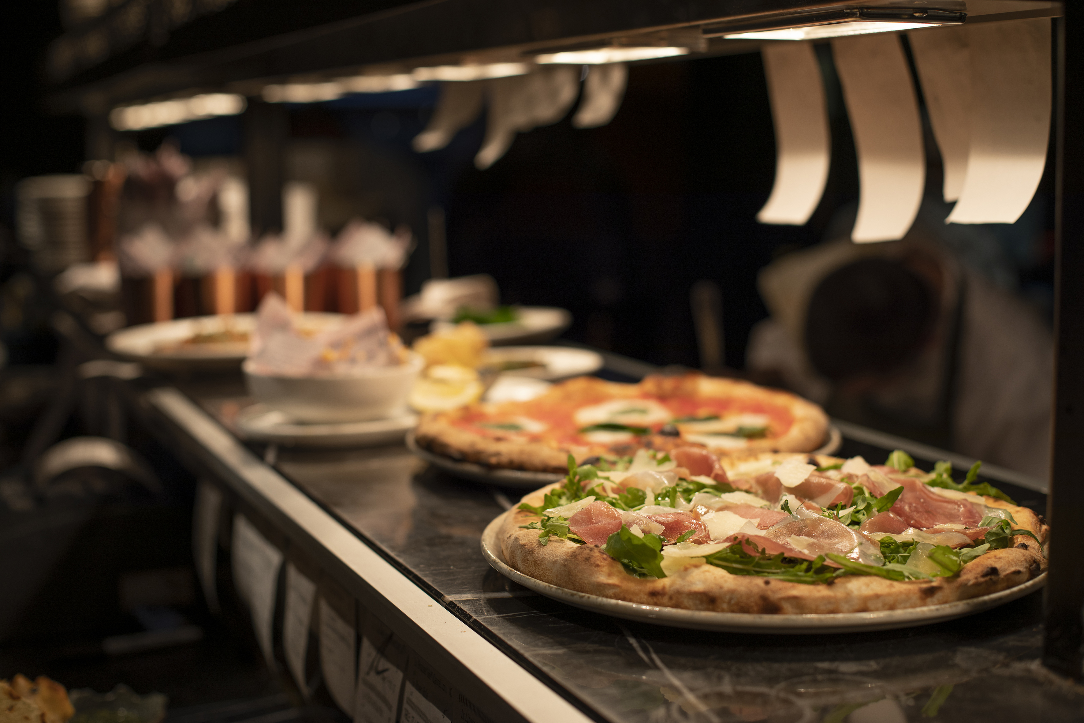Pizzas on restaurant counter: prosciutto, arugula, and Margherita style.